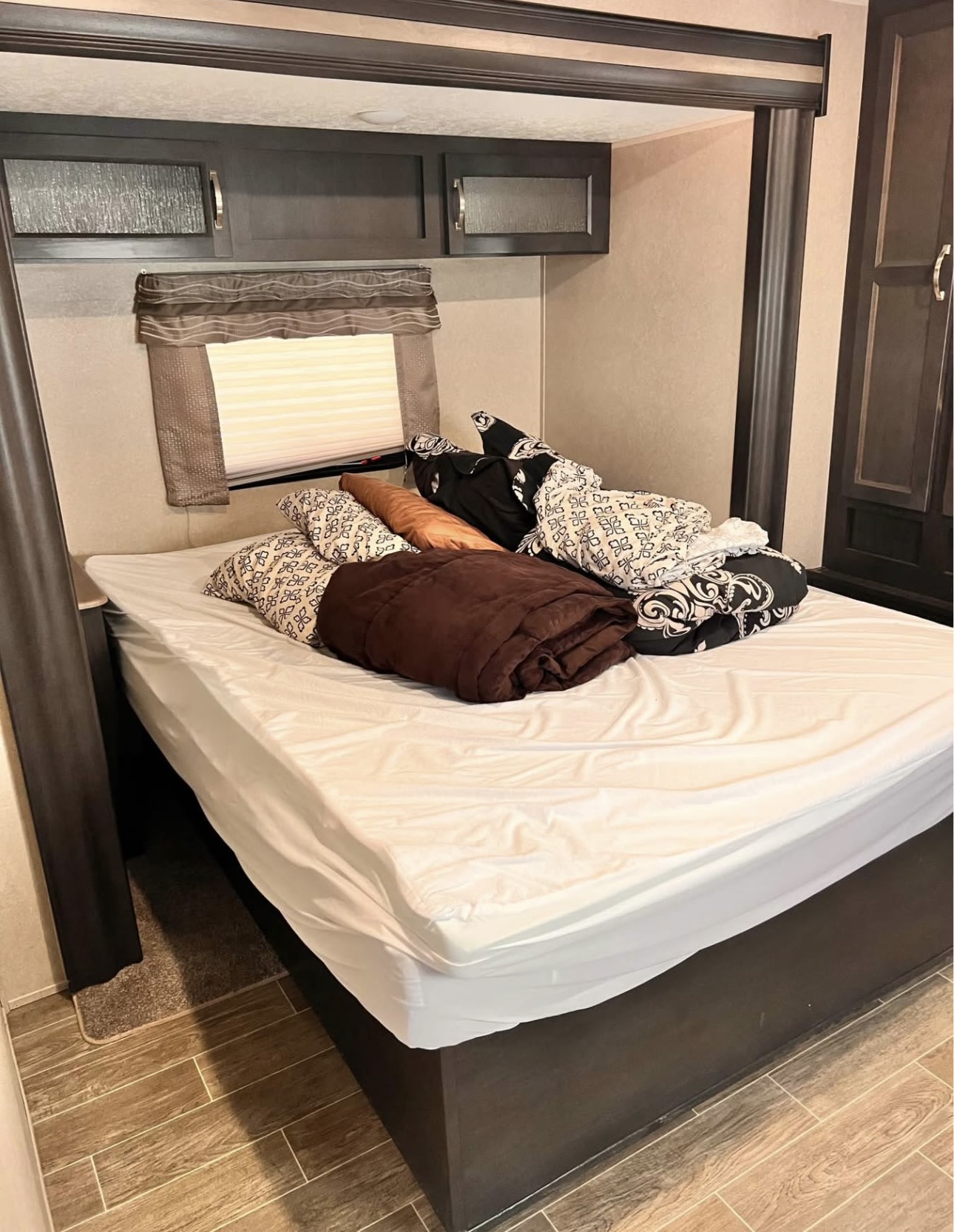 Cozy RV rental bedroom featuring a bed with white sheets, dark cabinets, window, and wood-look flooring.. Palomino 32RBFQ 2019