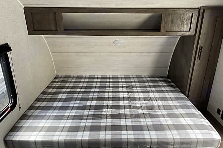 Cozy RV rental bedroom featuring a plaid bed, overhead storage, and wardrobe, ideal for travel and adventures.. Forest River Salem FSX 2021