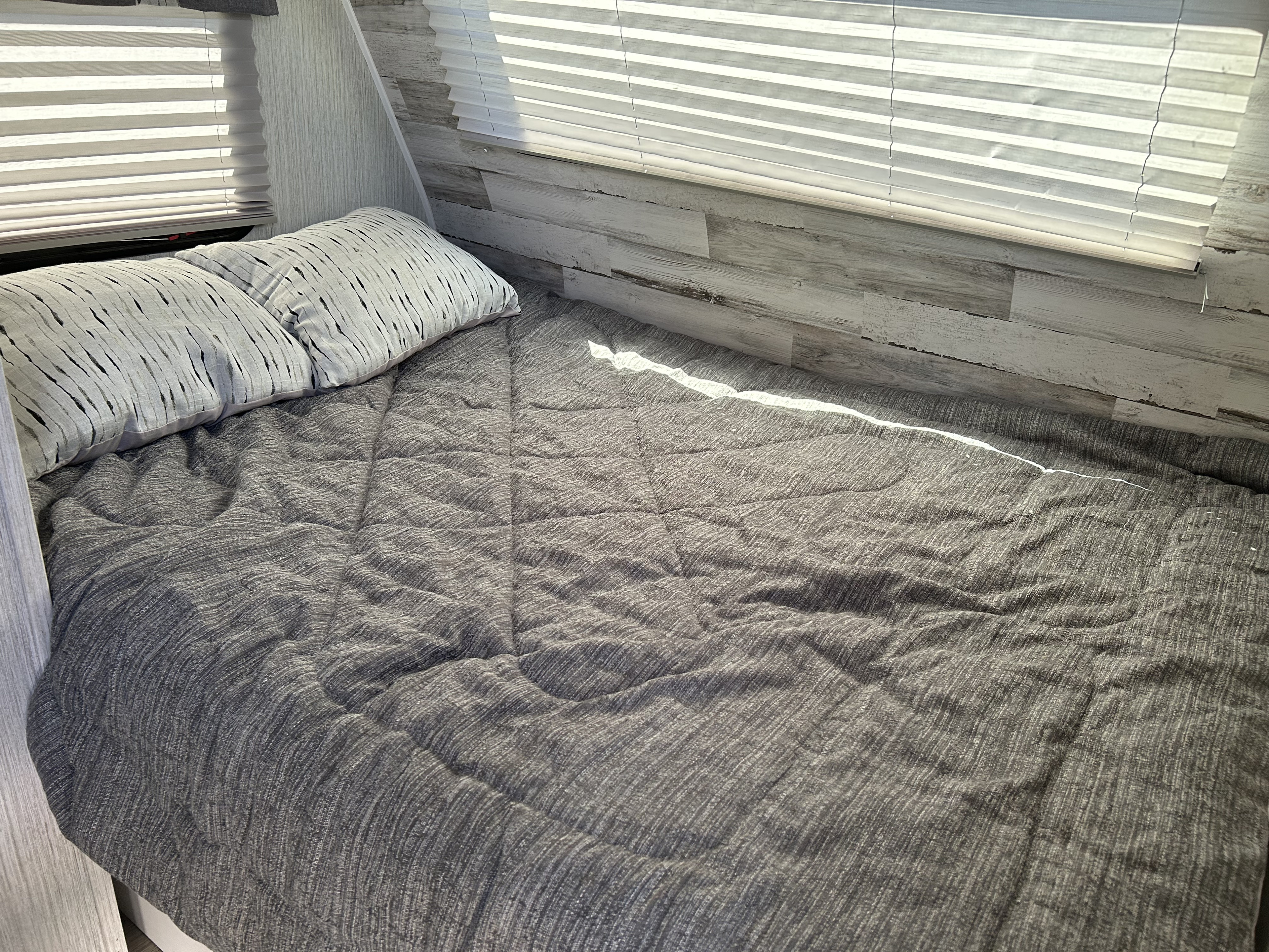 Cozy gray bed with decorative pillows and window blinds inside an RV rental bedroom, featuring whitewashed wood walls.. Palomino Puma 2022
