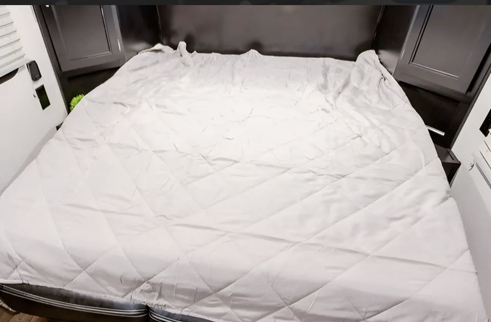 RV rental bedroom: A bright, neatly made bed with a quilted comforter, flanked by built-in storage and window blinds.. Forest River Cherokee Wolf Pup 2022