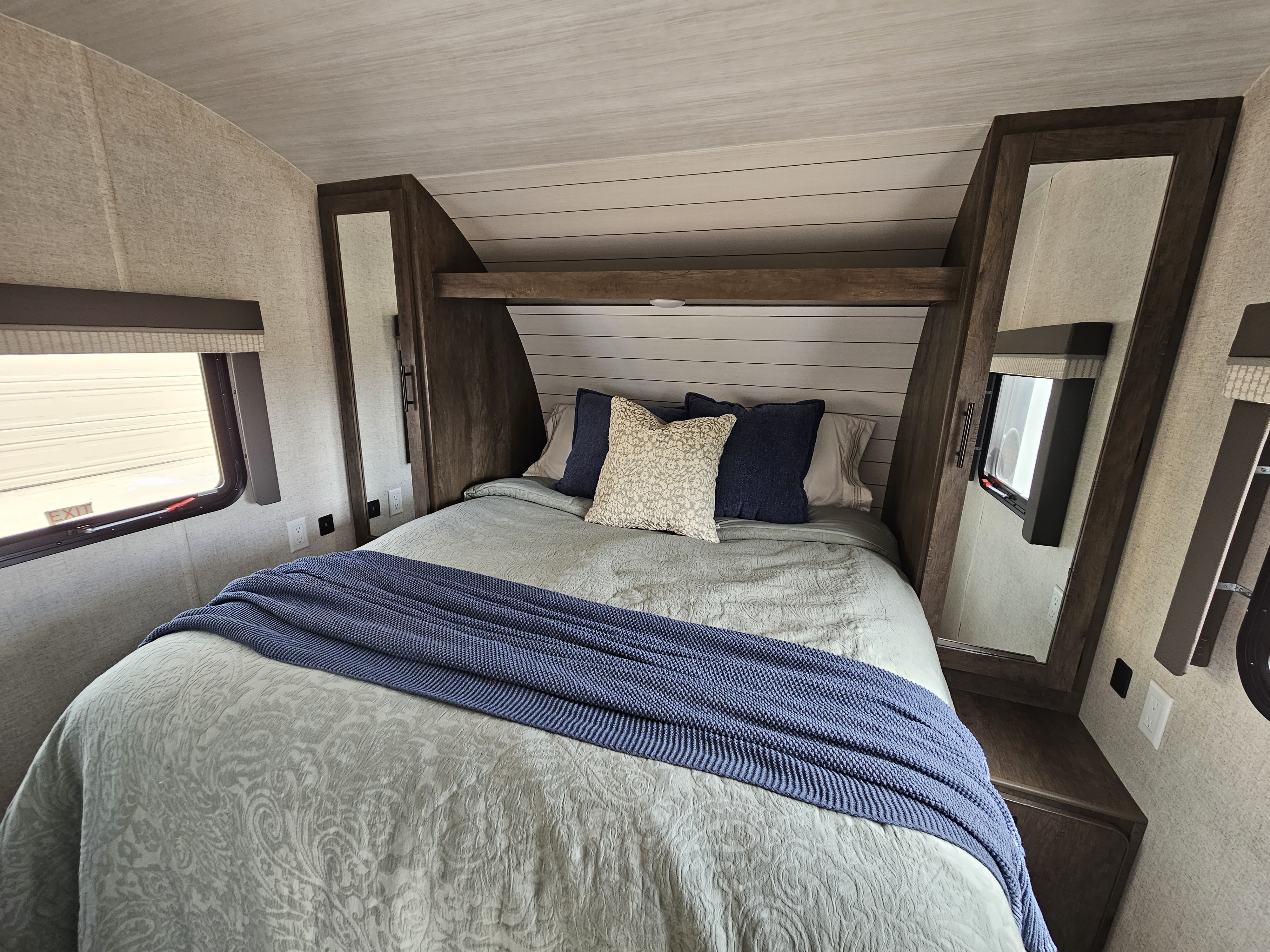 Spacious RV rental bedroom with comfy bed, blue throw, built-in wardrobes, and natural light from windows.. Forest River Wildwood X-Lite 2022