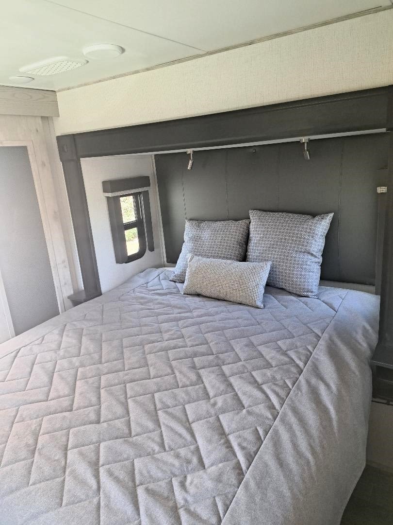 Comfortable RV rental bedroom with a large bed, grey quilted comforter, and patterned pillows. Dual reading lights above the dark headboard.. Keystone RV Alpine 2022