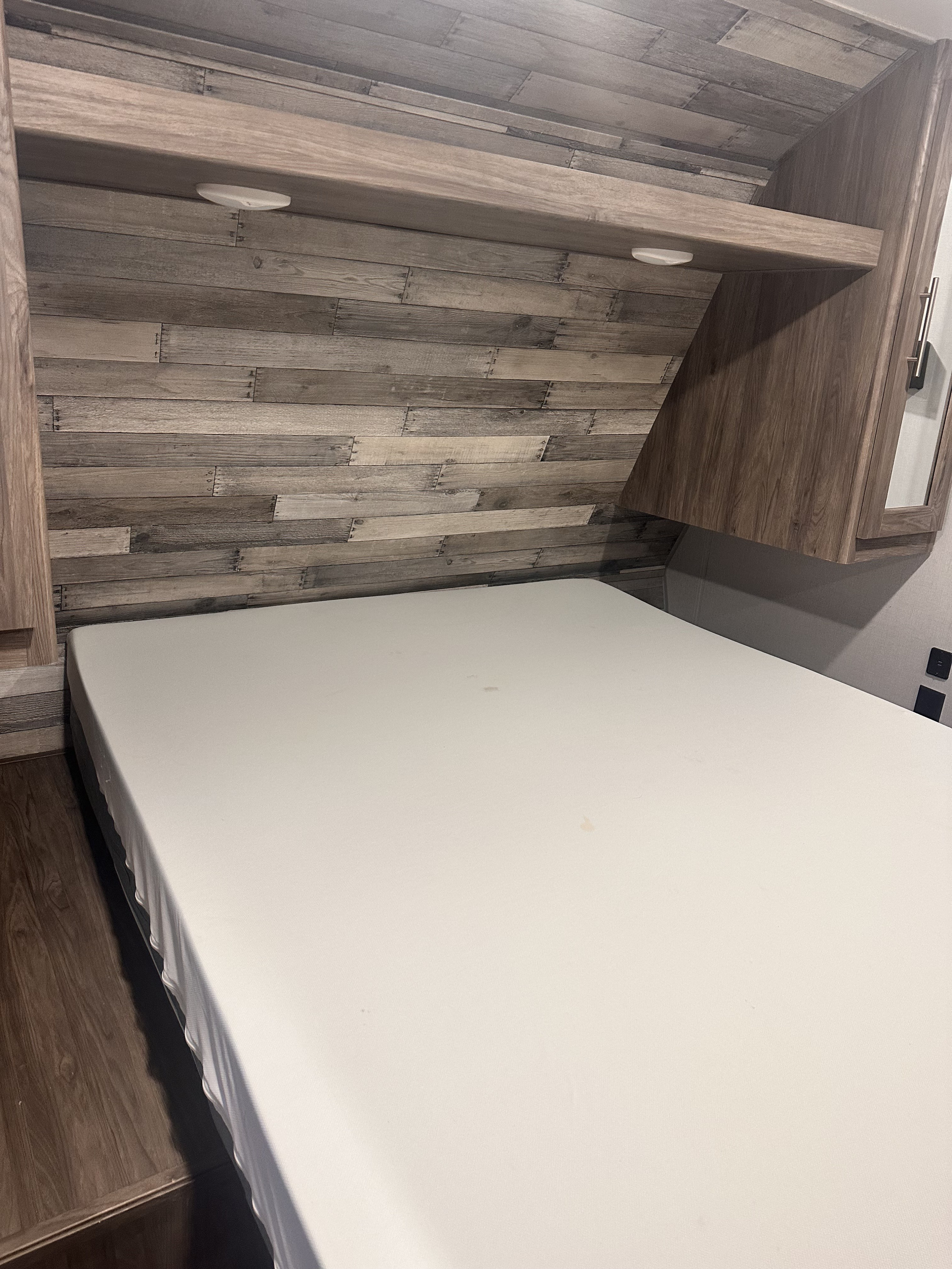 RV rental interior: a cozy bedroom with a clean mattress, rustic wood paneling, overhead shelf, and reading lights.. Crossroads RV Zinger 2020