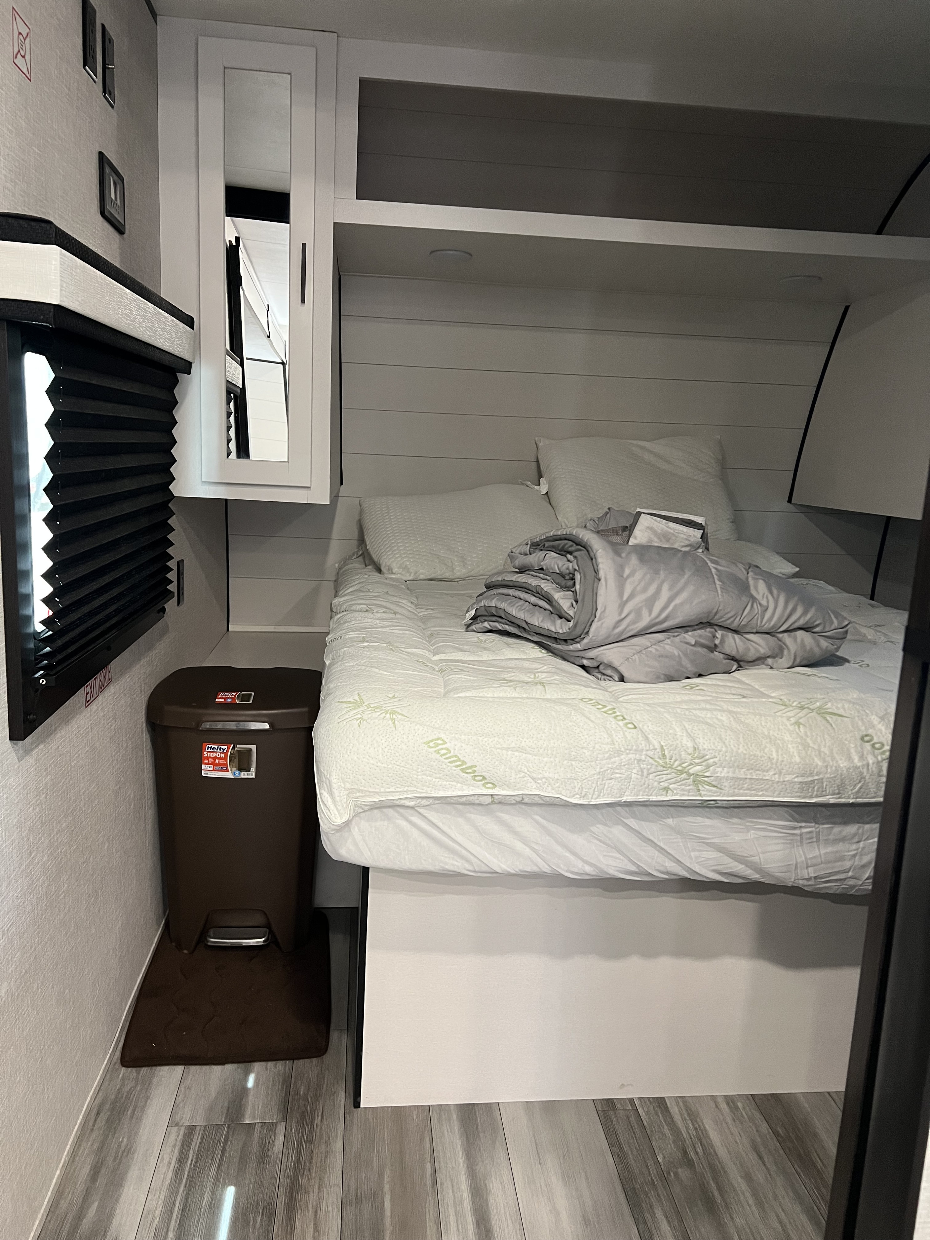 This cozy RV rental bedroom features a comfortable bed, white shiplap walls, cabinet, and a convenient trash bin.. Jayco Jay Flight 2024