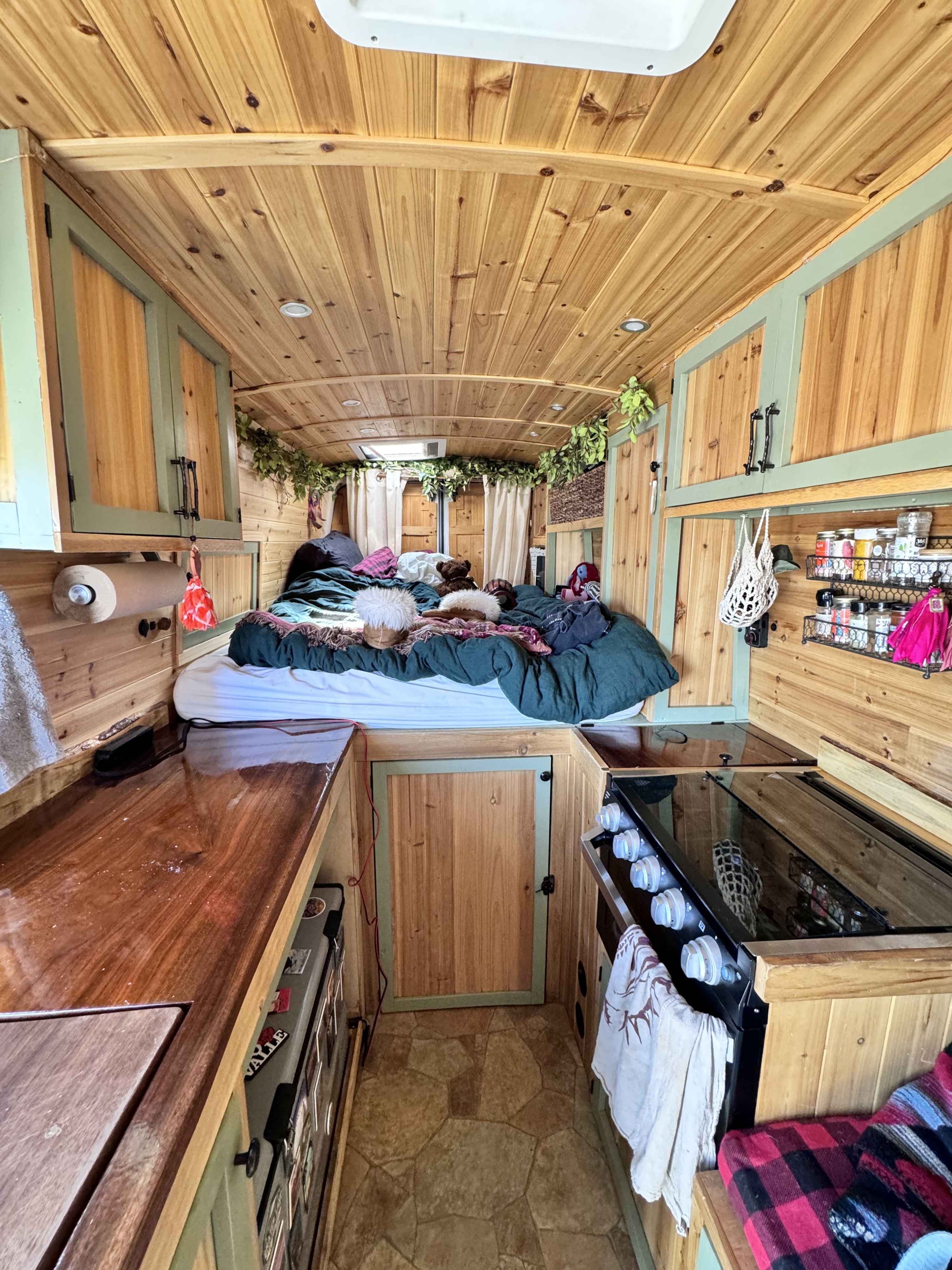 Step into this cozy wood-paneled RV rental: a comfy bed, compact kitchen, green accents, and ambient overhead lights.. Ford Transit 2015