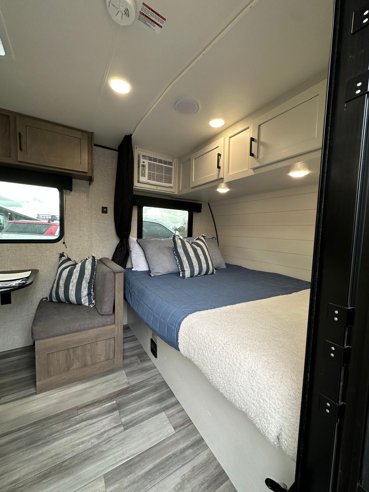 Experience an RV rental's cozy interior, featuring a comfortable bed, dinette, and overhead storage for your travels.. Jayco Jay Flight SLX 2024