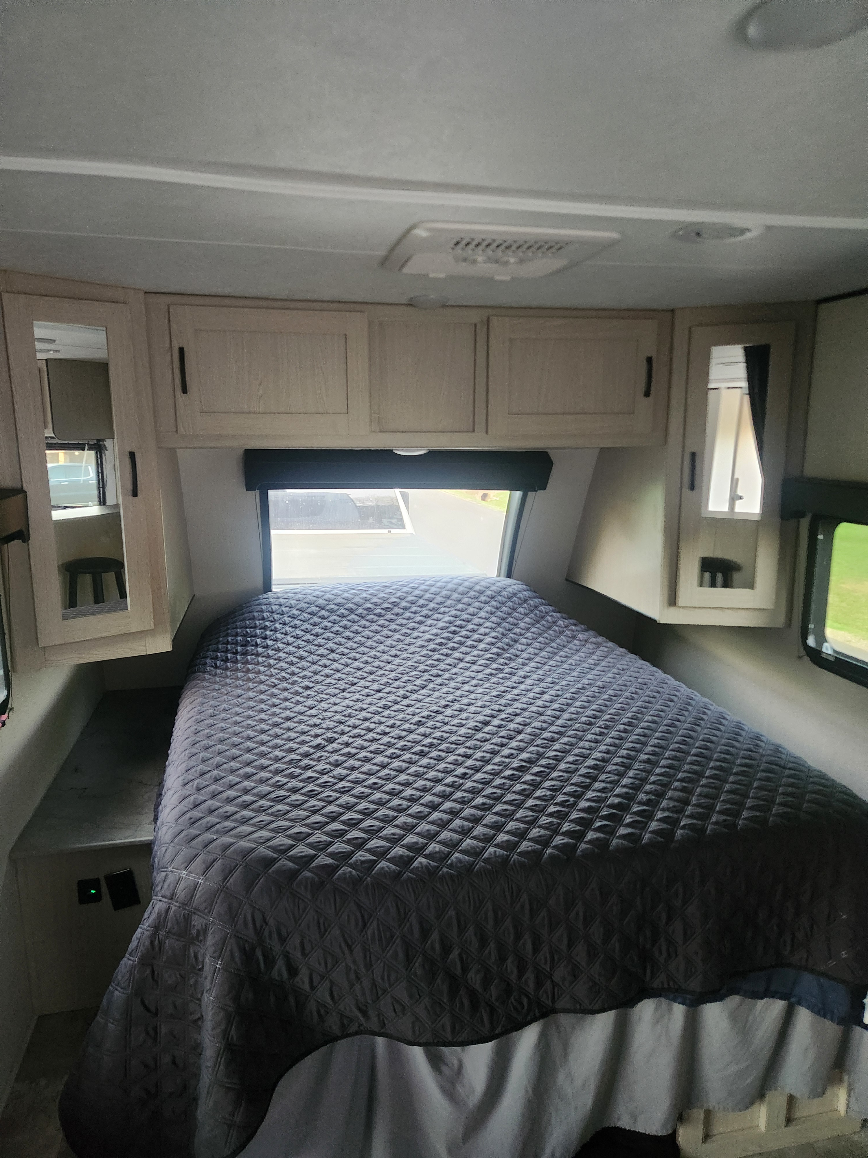 Spacious RV rental bedroom with a dark, quilted bed, light wood overhead cabinets, and windows. Cozy interior for travel.. Coachmen Apex 2022