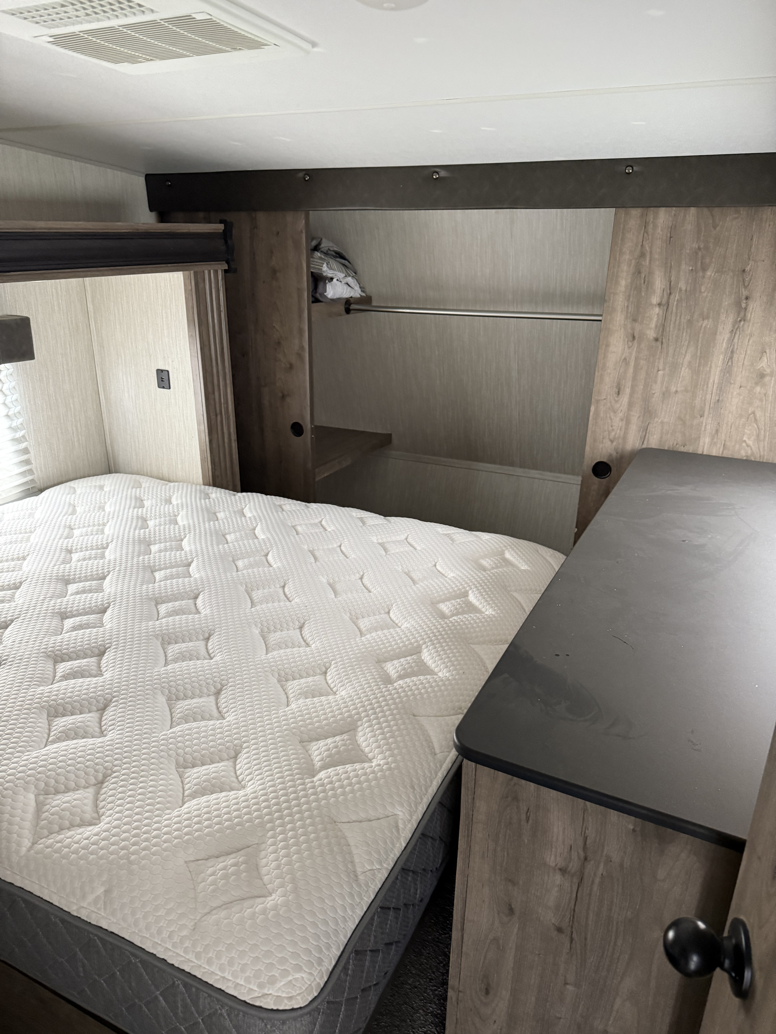 Cozy RV rental bedroom featuring a white quilted mattress, built-in wood-look storage, and an overhead AC unit for comfortable travel.. Forest River Vengeance Rogue Toy Hauler 2020