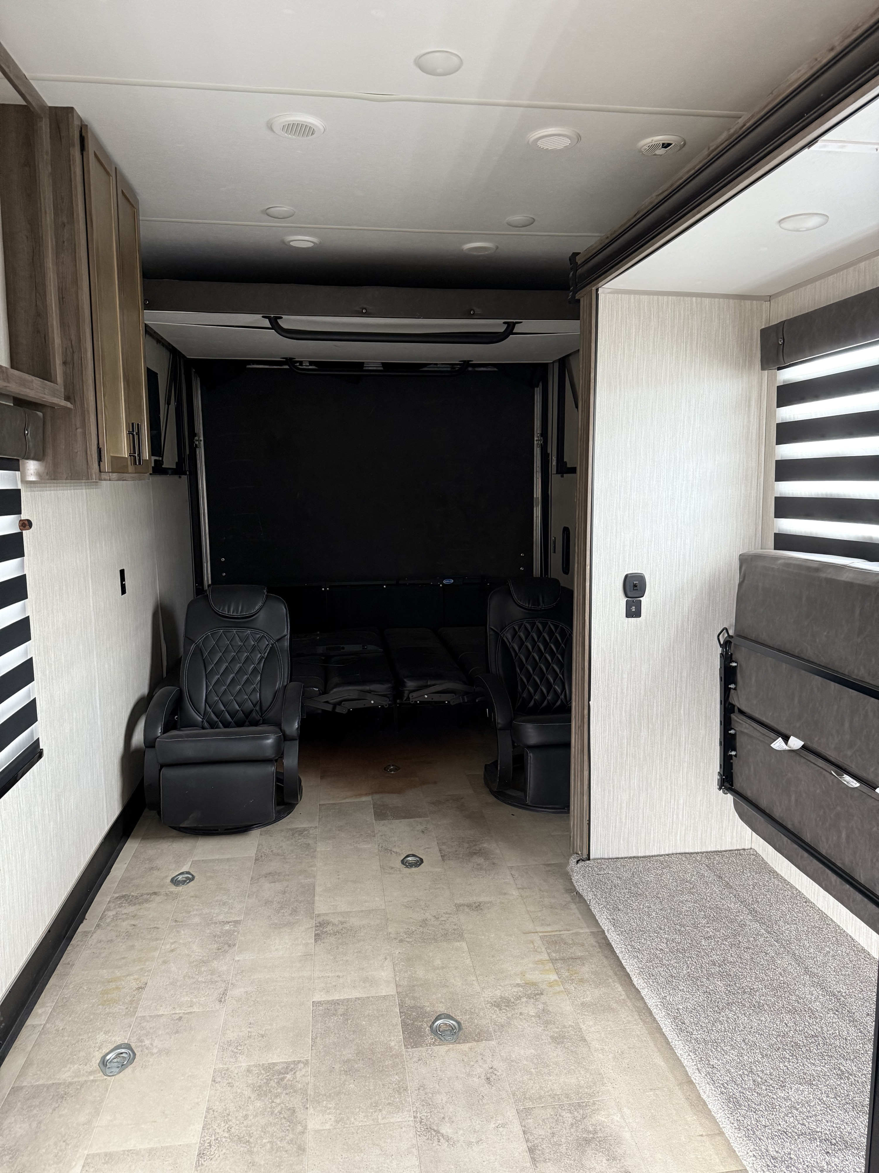 Inside this RV rental toy hauler: black recliners, fold-away bed, and tie-downs on a light floor.. Forest River Vengeance Rogue Toy Hauler 2020