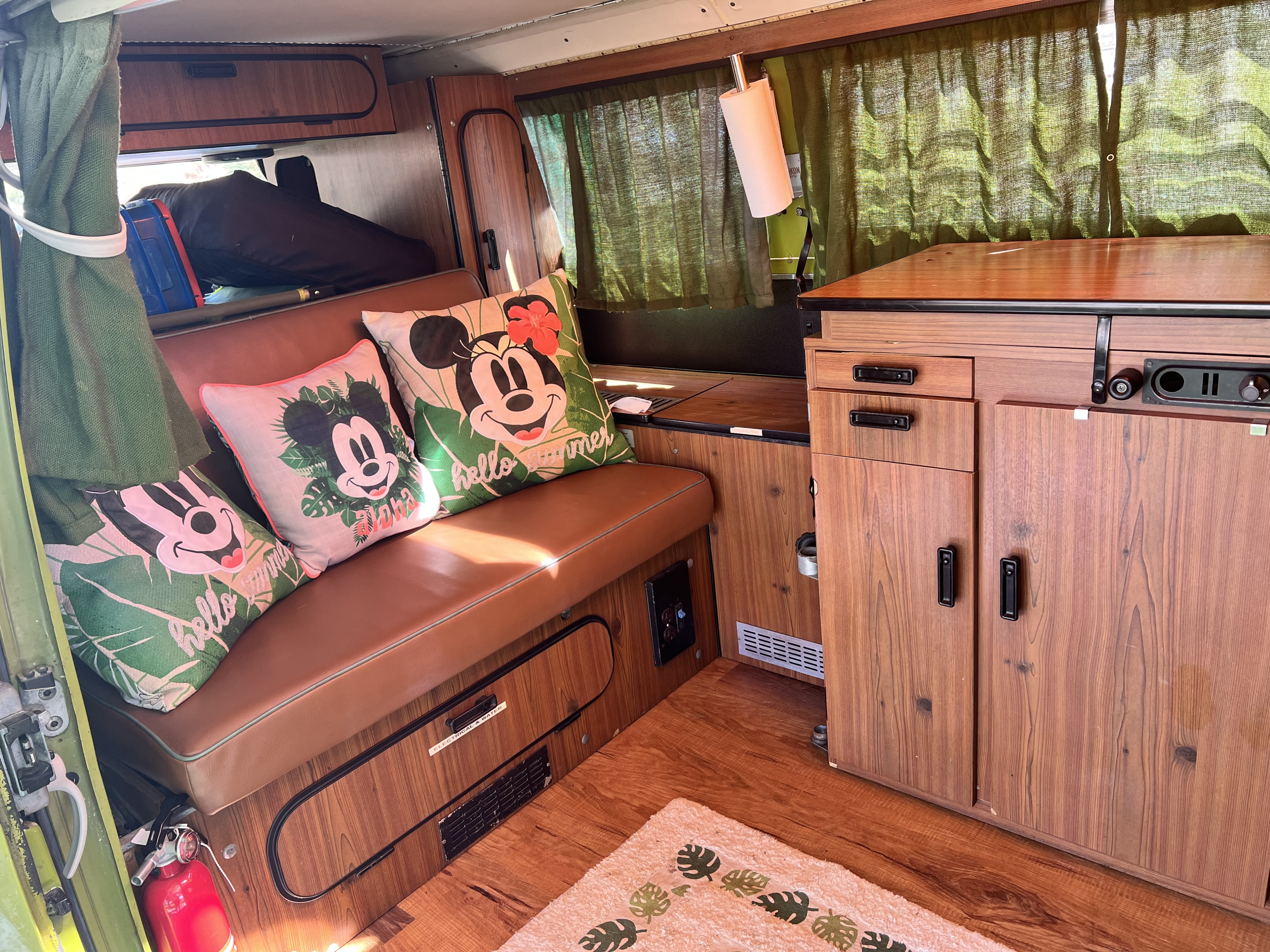 Inside a vibrant rv rental: brown seating, Mickey pillows, wood storage, and practical features like a fire extinguisher.. Volkswagen Kombi T2 Westfalia 1976