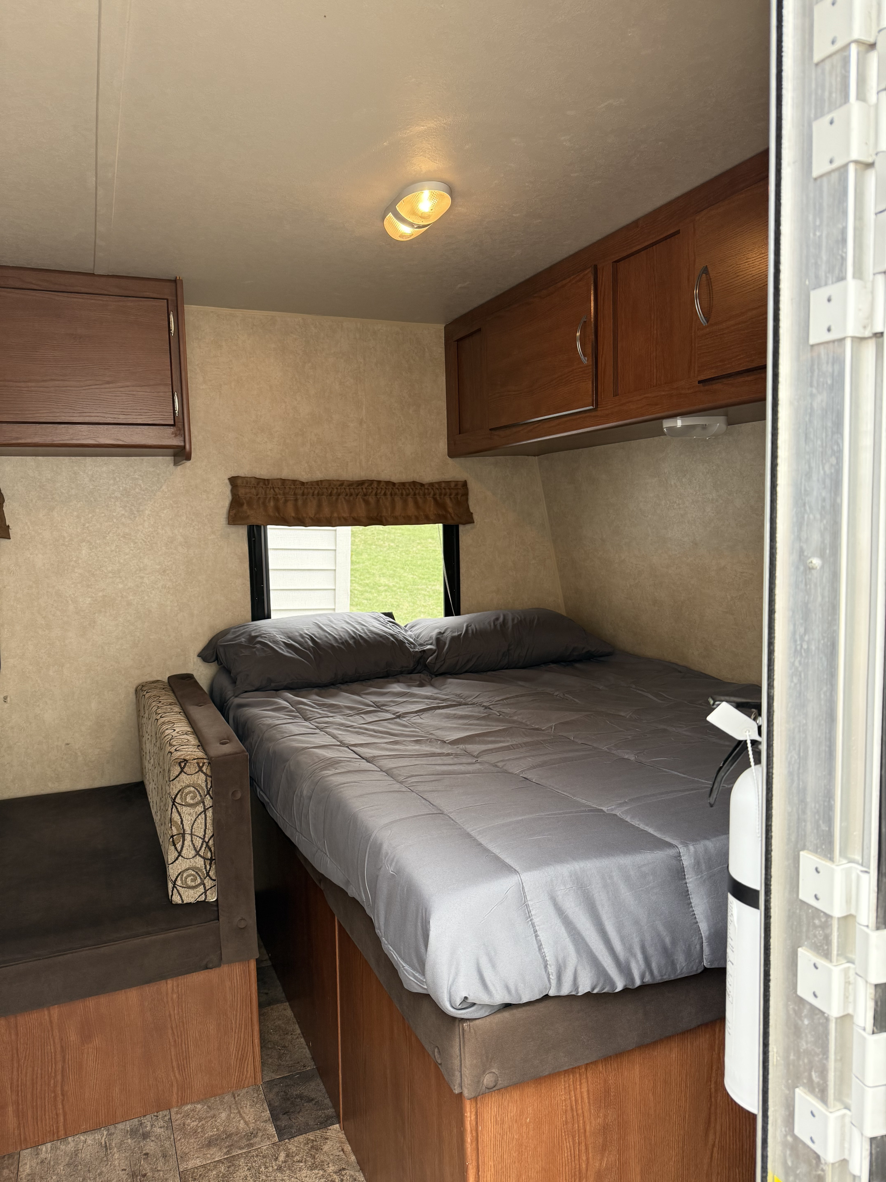 RV rental bedroom featuring a comfy bed with grey linens, overhead wood cabinets, and a window view.. Forest River Wildwood X-Lite FS 2015