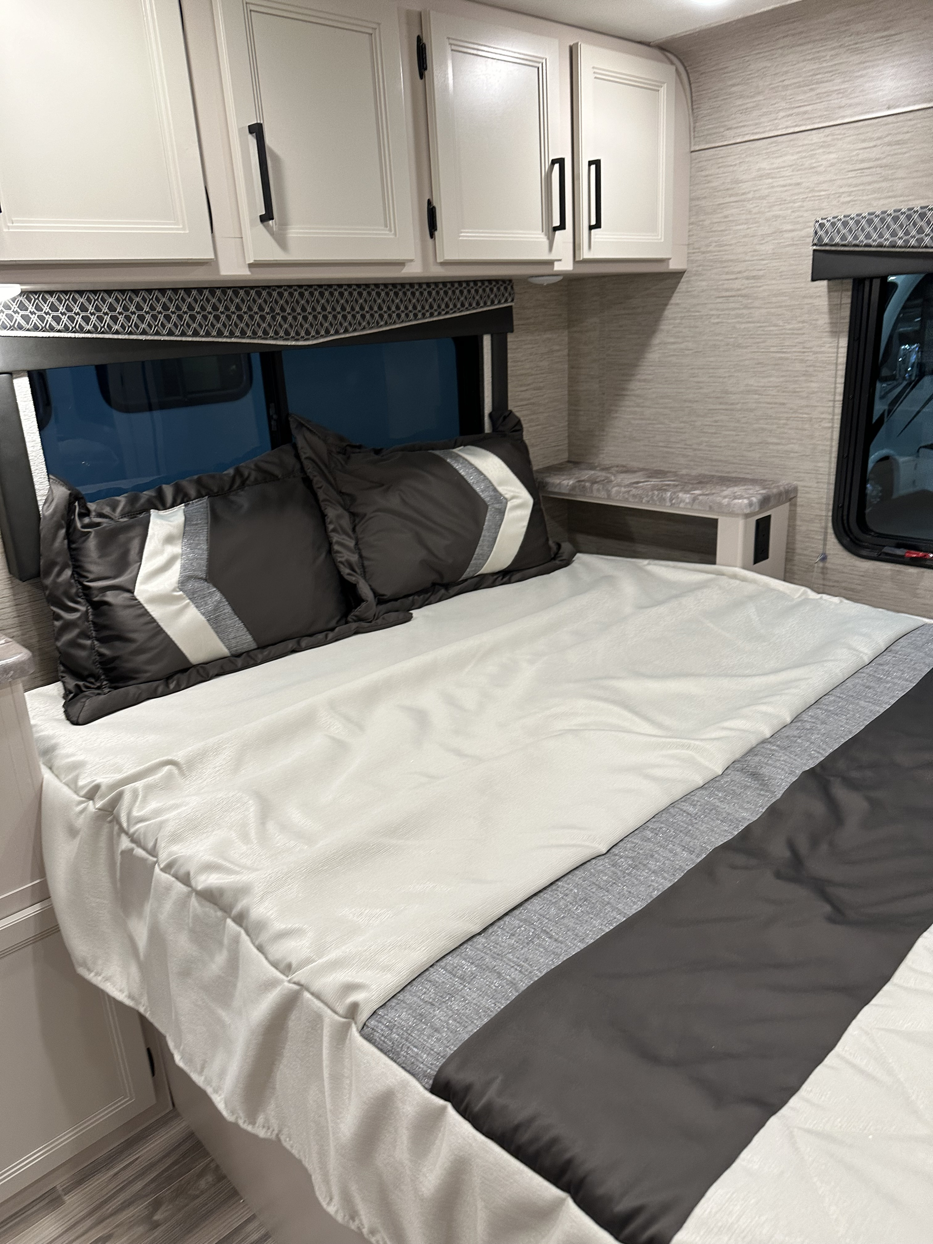 Step inside this cozy RV rental bedroom. Features a comfortable bed with stylish pillows, overhead cabinets, and a bedside shelf.. Coachmen Pursuit 2023