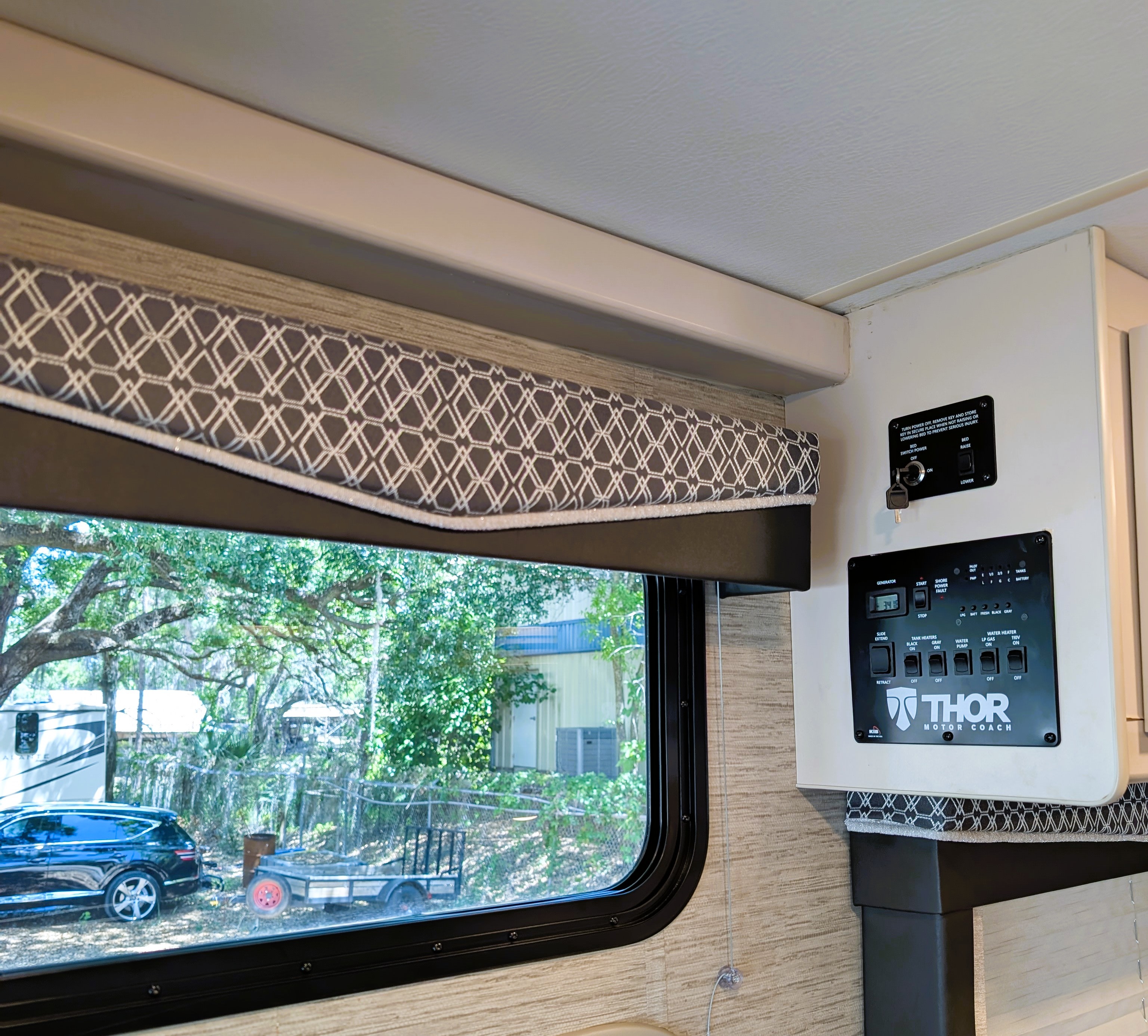 RV rental interior: control panels for bed lift, generator, and water systems.. Thor Motor Coach A.C.E 2023