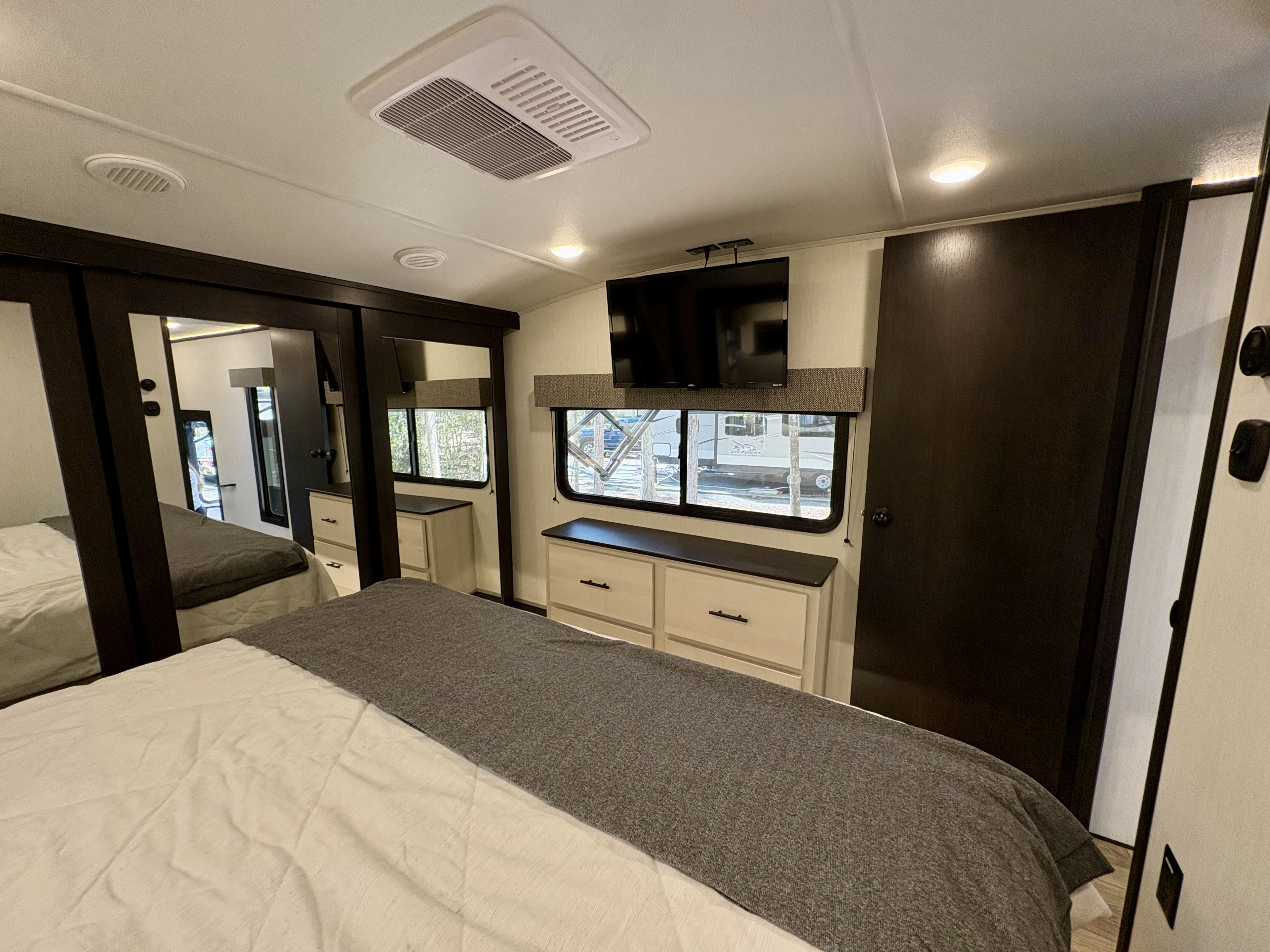 Well-appointed RV rental bedroom featuring a comfortable bed, mirrored closet, TV, and outdoor views.. Forest River Sabre Cobalt 2025