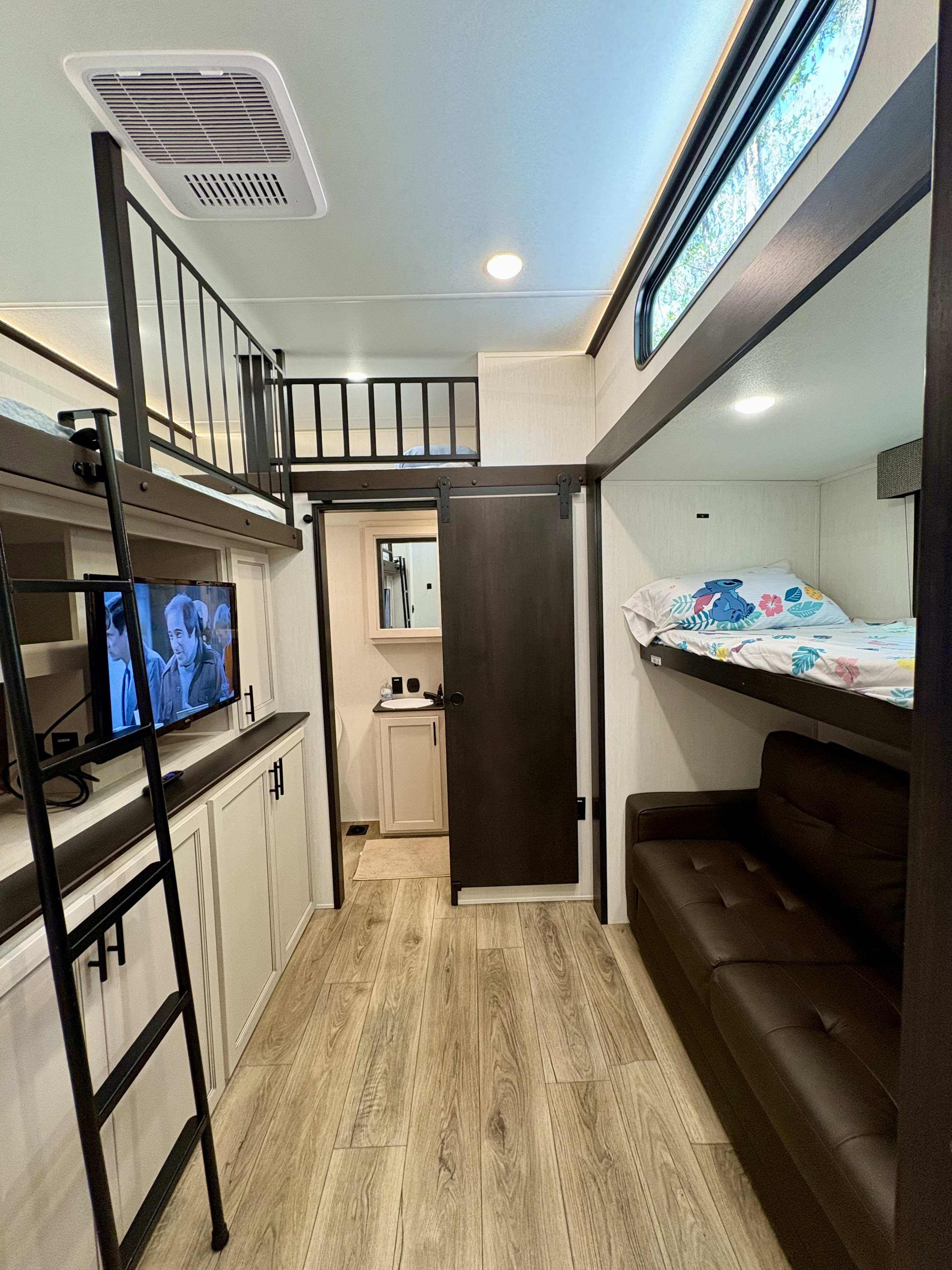 Cozy RV rental interior with bunk beds, a loft, sofa, TV area, and sliding bath door.. Forest River Sabre Cobalt 2025