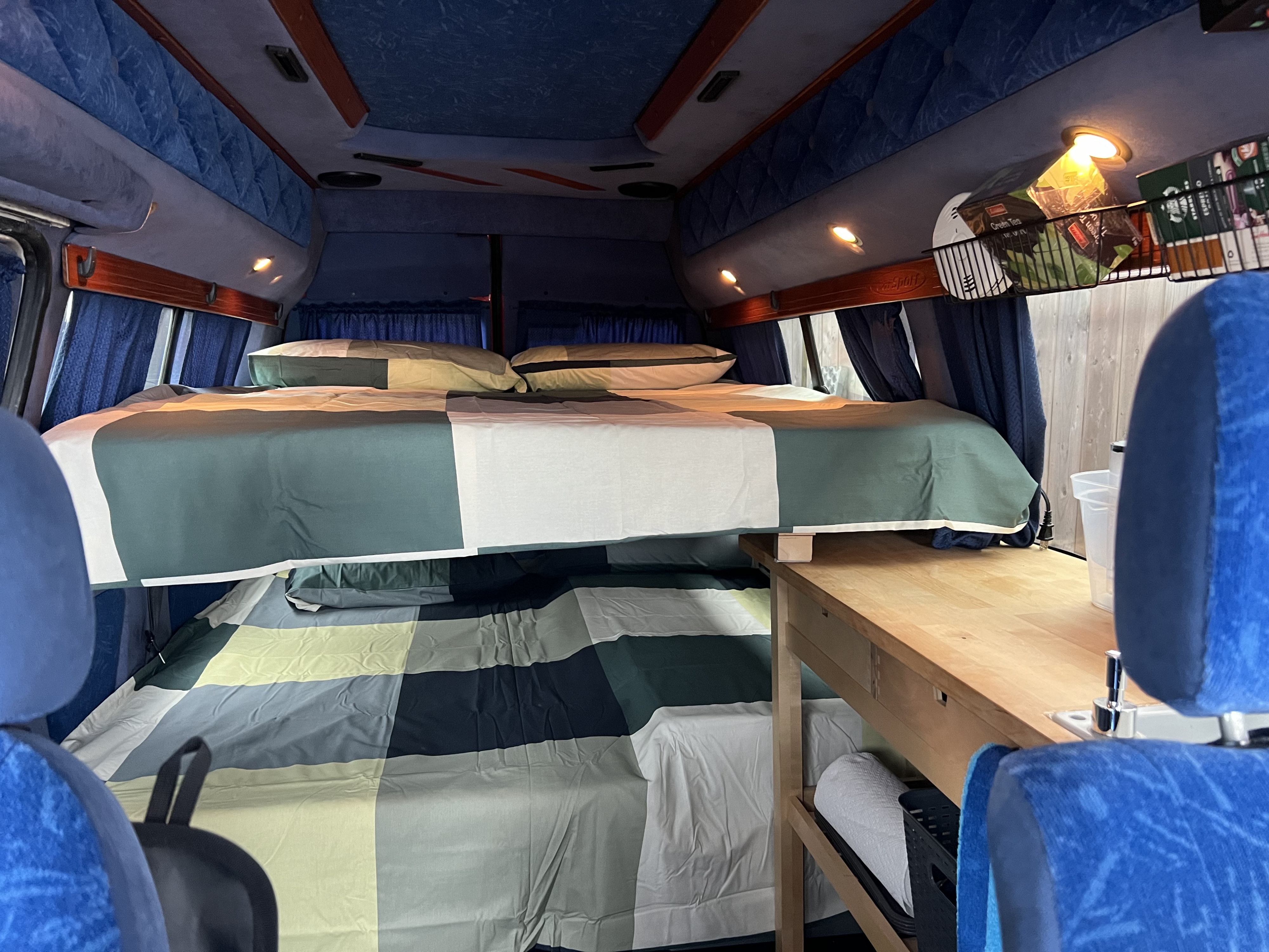 This RV rental features a cozy camper interior with stacked bunk beds, a kitchen counter, and overhead storage.. Volkswagen Multivan 2003