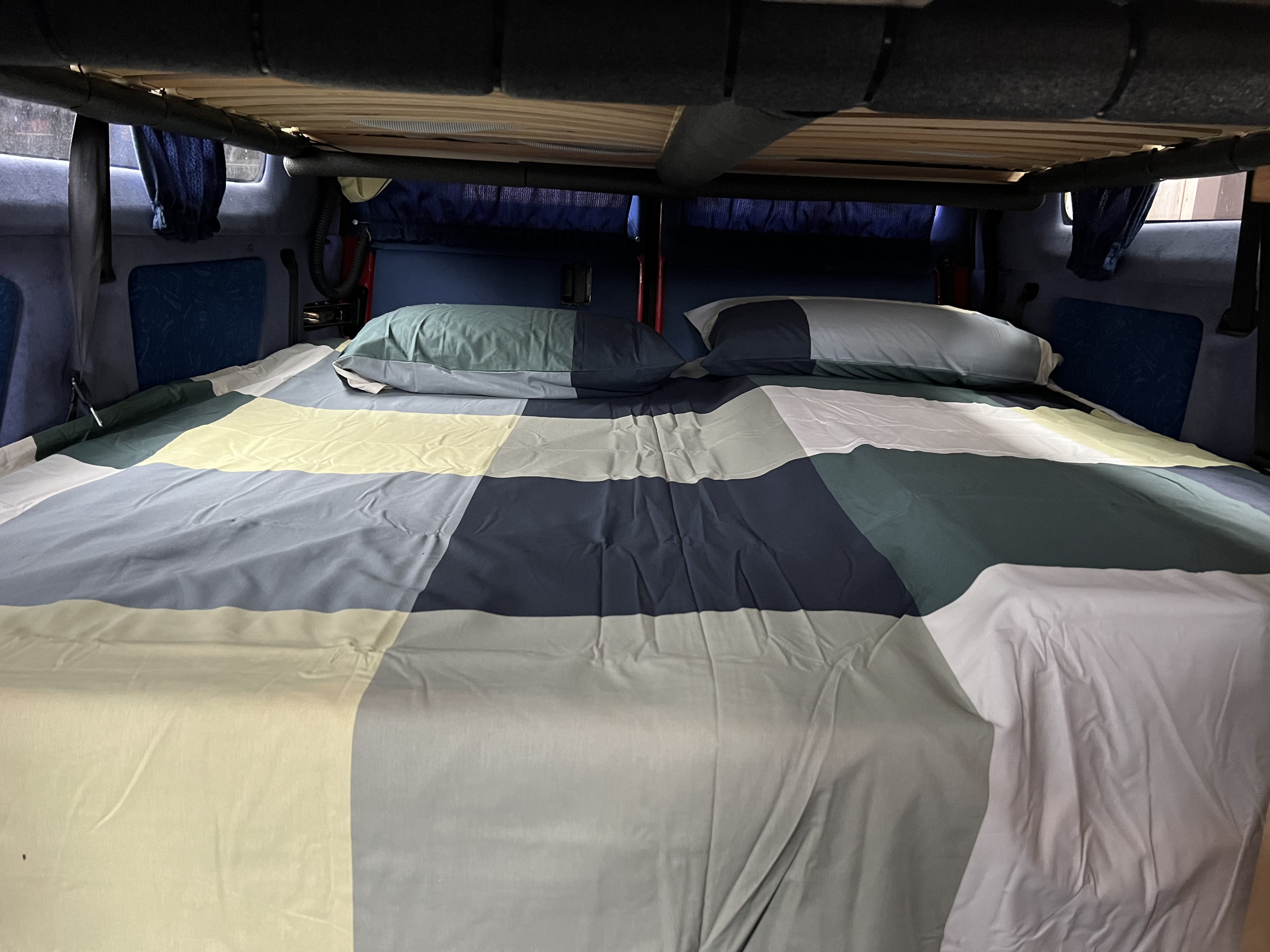 Cozy RV rental sleeping area with patchwork bedding and pillows, perfect for road trips.. Volkswagen Multivan 2003
