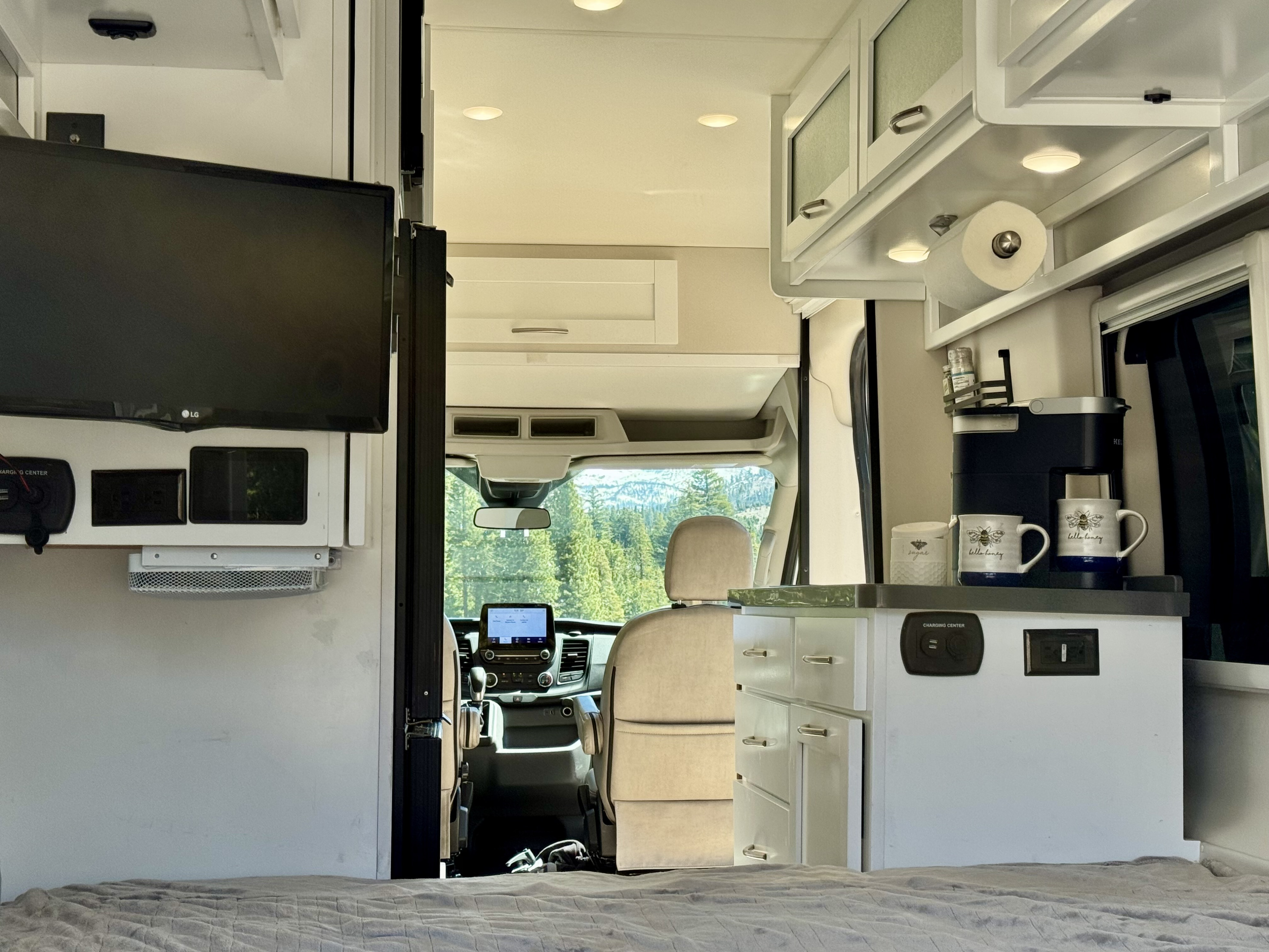 Inside a modern RV rental: comfortable bed, kitchen, TV, and forest views for your adventure.. Coachmen Beyond 2021