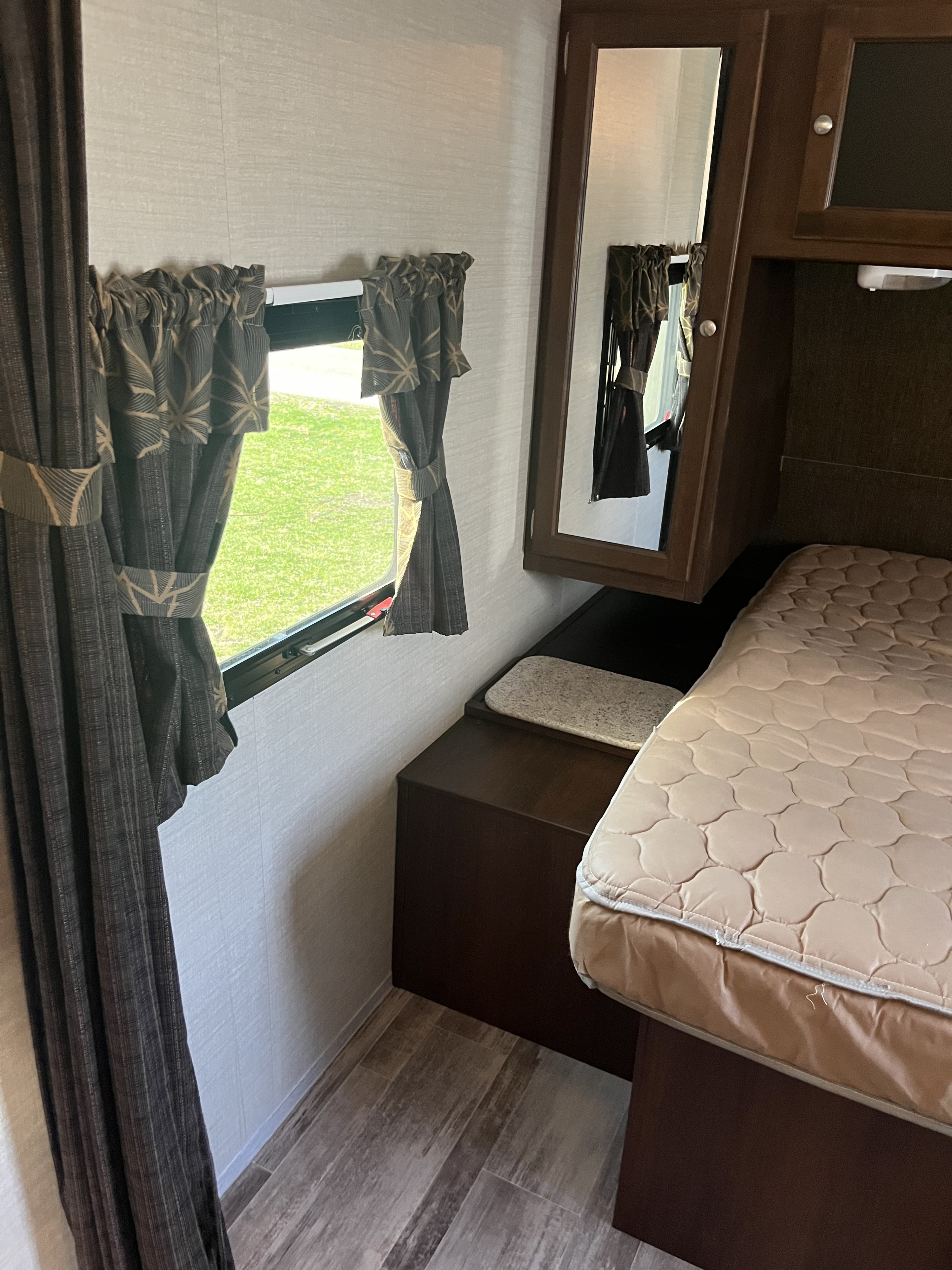RV rental interior: cozy bedroom with quilted bed, window, dark curtains, wood cabinets, and mirror.. Keystone RV Bullet Ultra Lite 2015