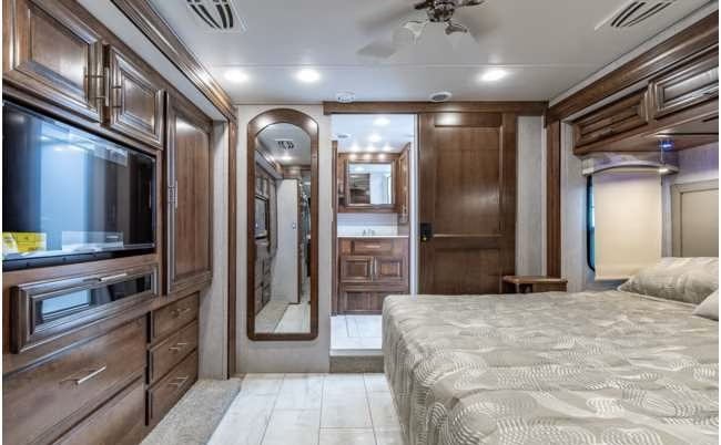 Spacious RV rental bedroom with a large bed, TV unit, wood storage, and an attached vanity/bathroom.. Forest River BERKSHIRE 2022