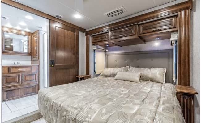 Spacious RV rental bedroom with rich wood cabinetry, a large bed, and an adjacent bathroom, showcasing comfortable travel.. Forest River BERKSHIRE 2022