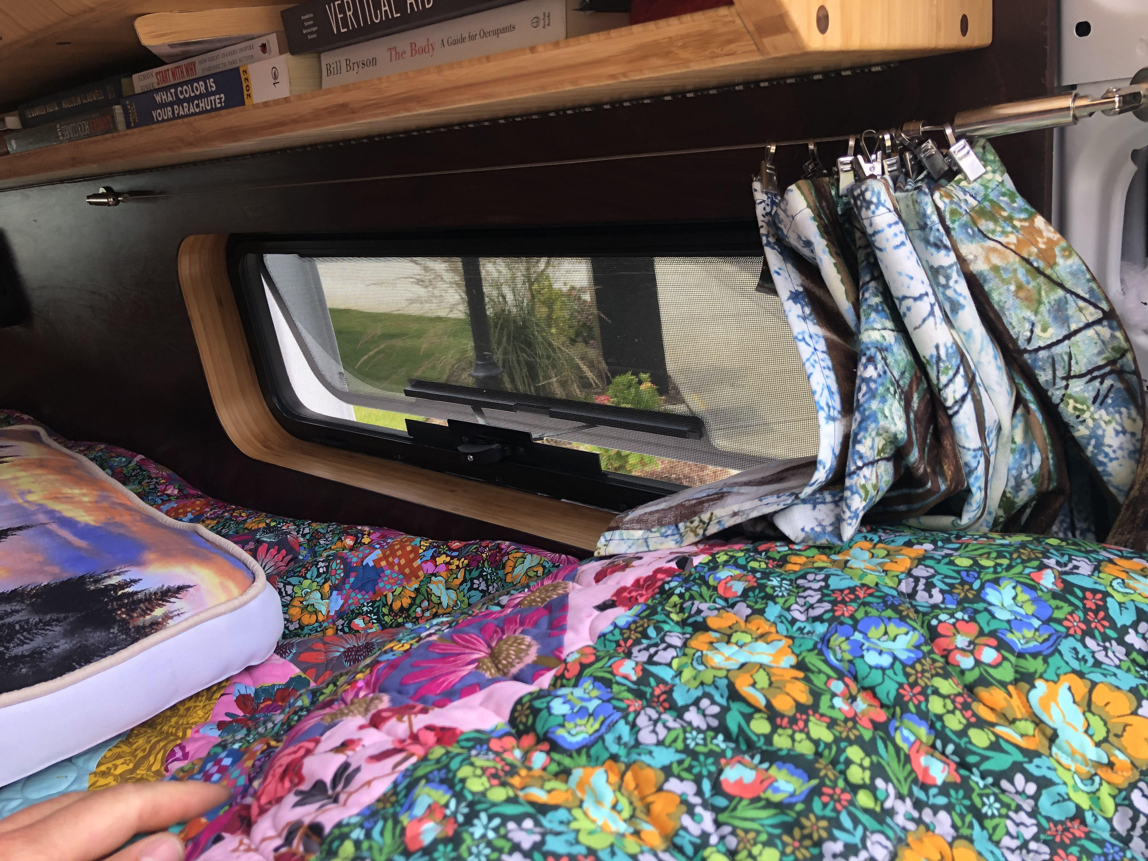 Relaxing RV rental interior: colorful quilted bed, window, and books on a shelf for cozy travels.. Ram promaster 2500 2017