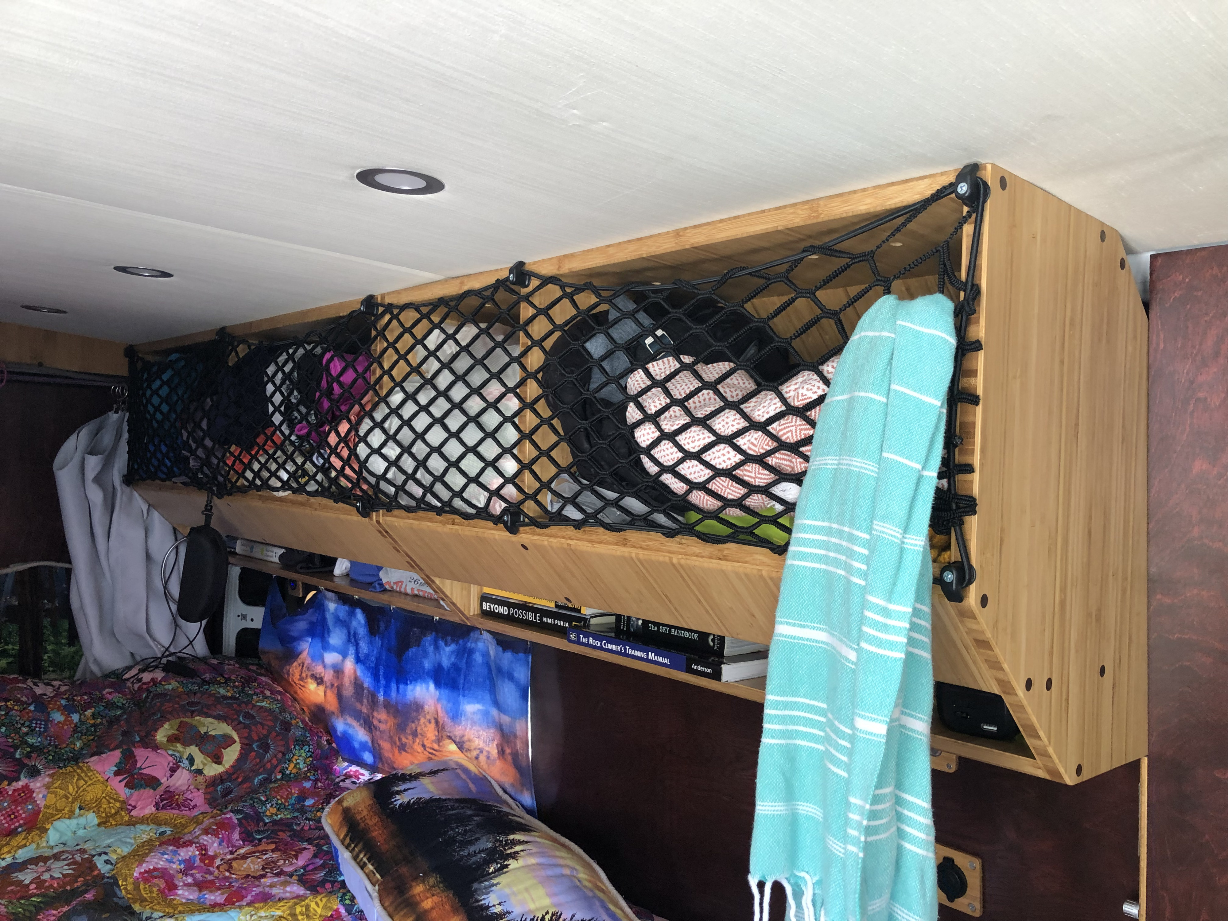 Inside an RV rental: view of a clever overhead storage net filled with essentials above a cozy bed and books.. Ram promaster 2500 2017