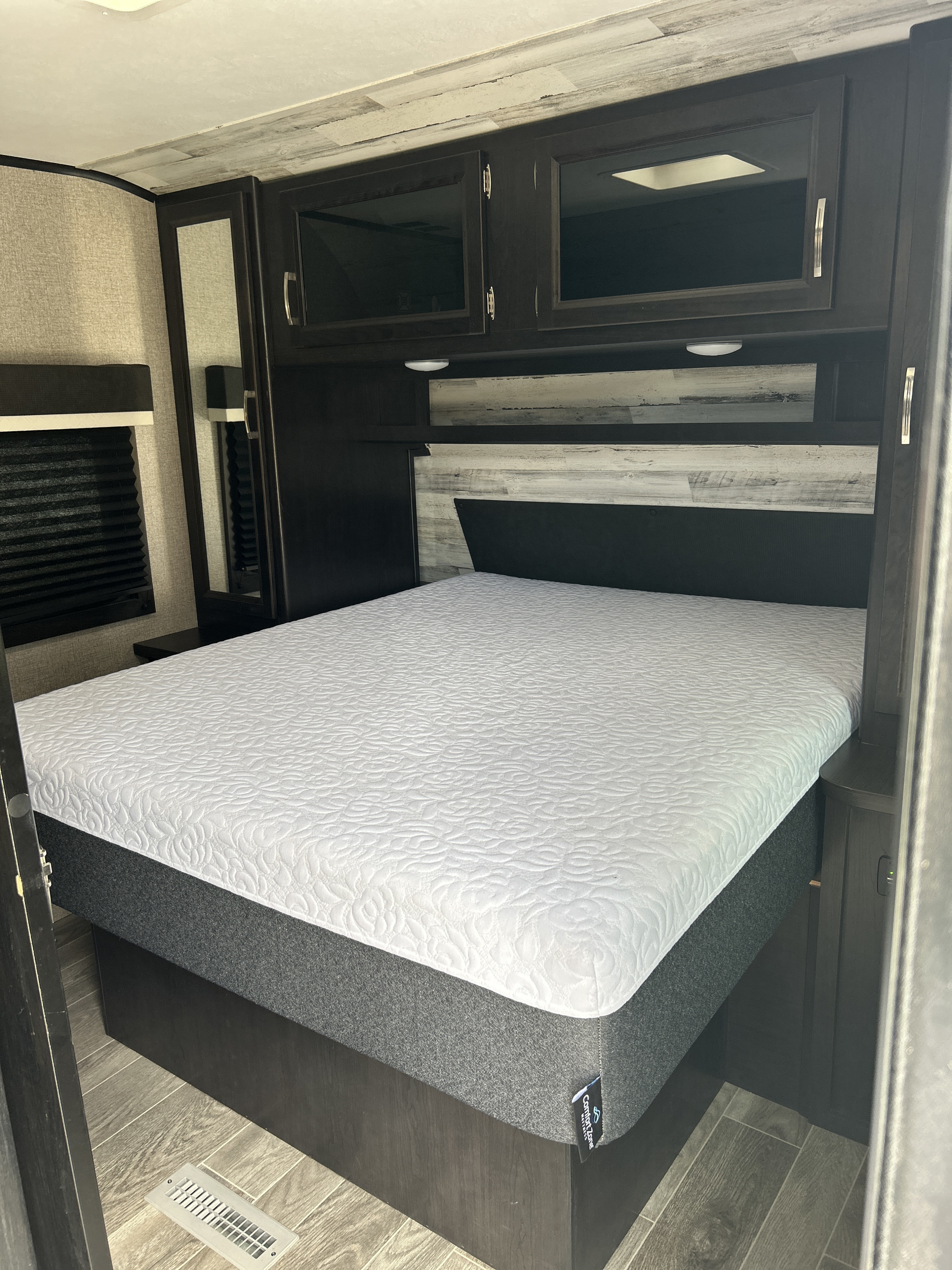 Cozy RV rental bedroom with a comfy ComfortZone mattress, dark cabinetry, and mirror, perfect for travel.. Jayco Jay Feather 2021