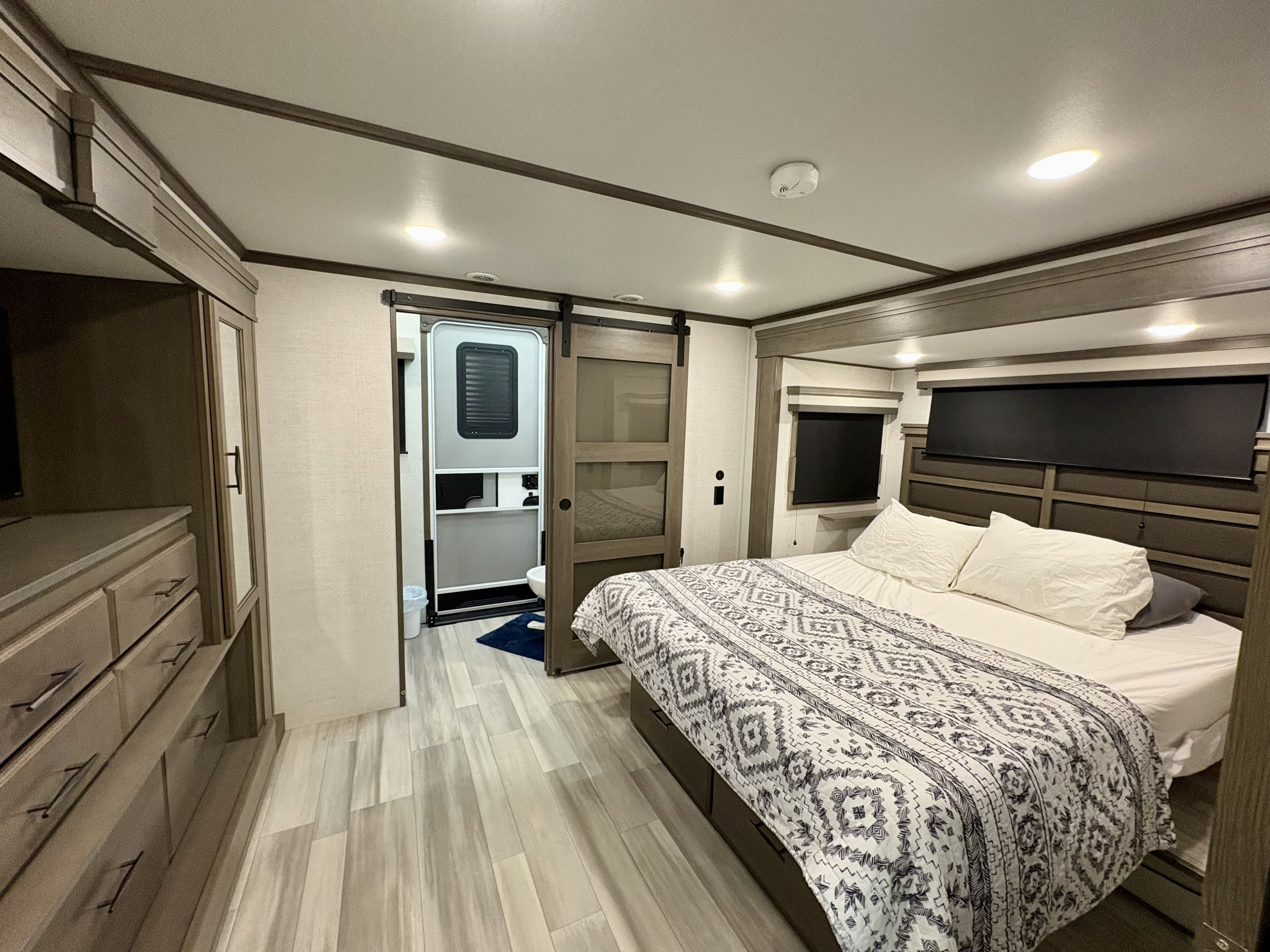 Enjoy a comfortable RV rental bedroom, featuring a queen bed, modern storage, and an attached bath.. Grand Design Solitude 2023