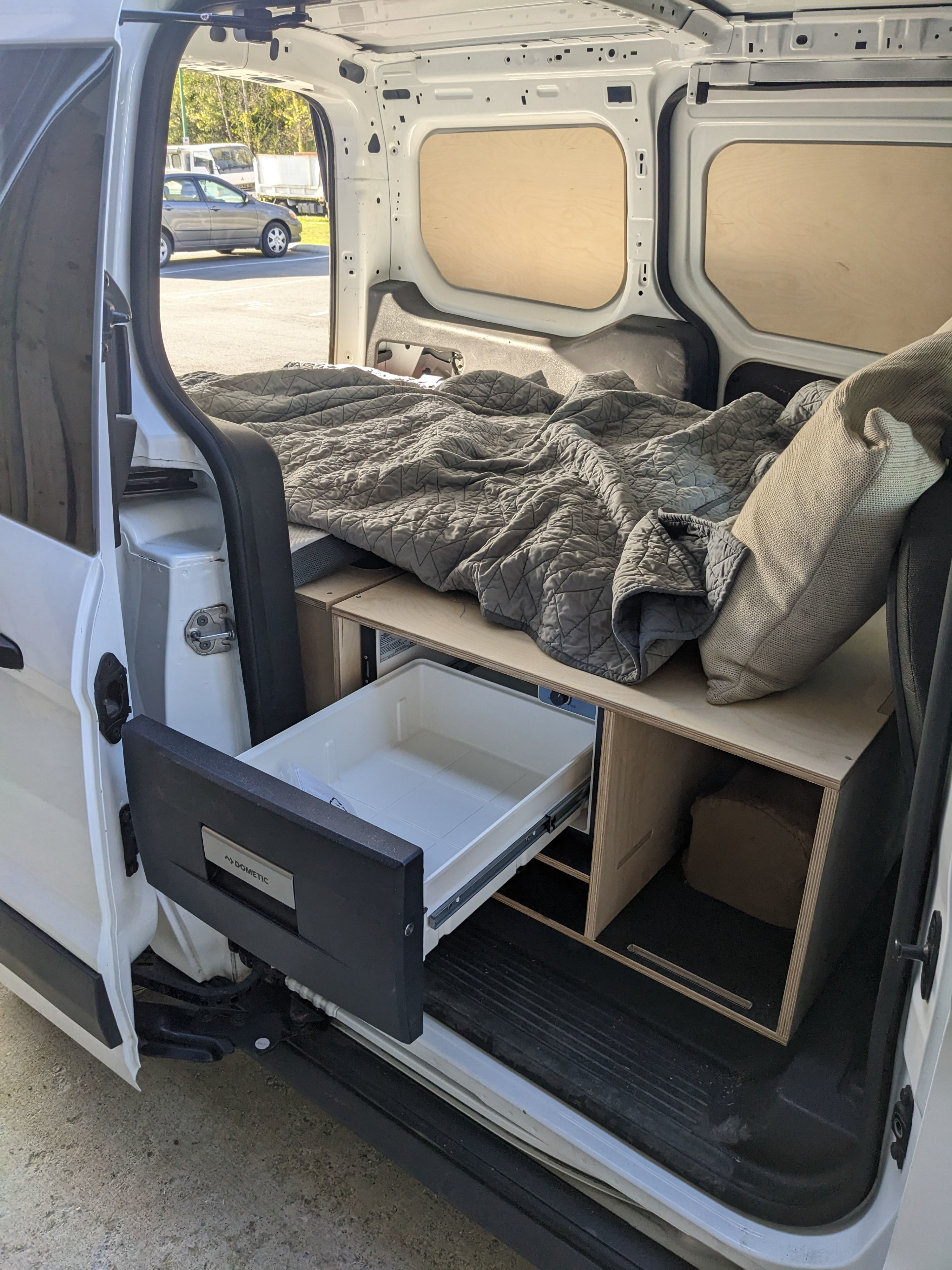 This rv rental van conversion interior features a custom bed, a Dometic drawer fridge, and storage for mobile living.. Ford Transit 2015