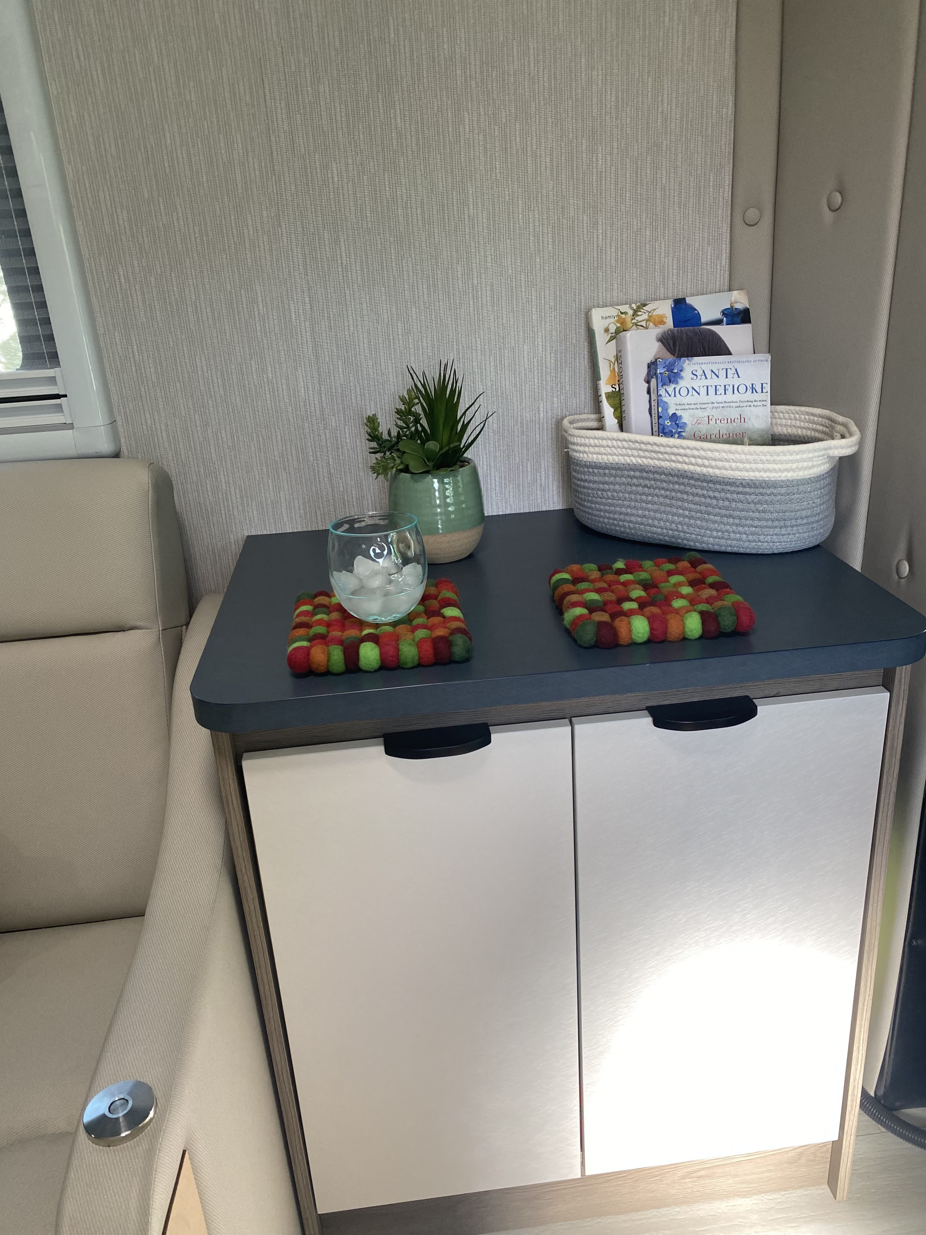 Cozy and organized RV interior with a side table, plant, books, and colorful coasters. Perfect for an RV rental getaway.. Ford Transit 2023
