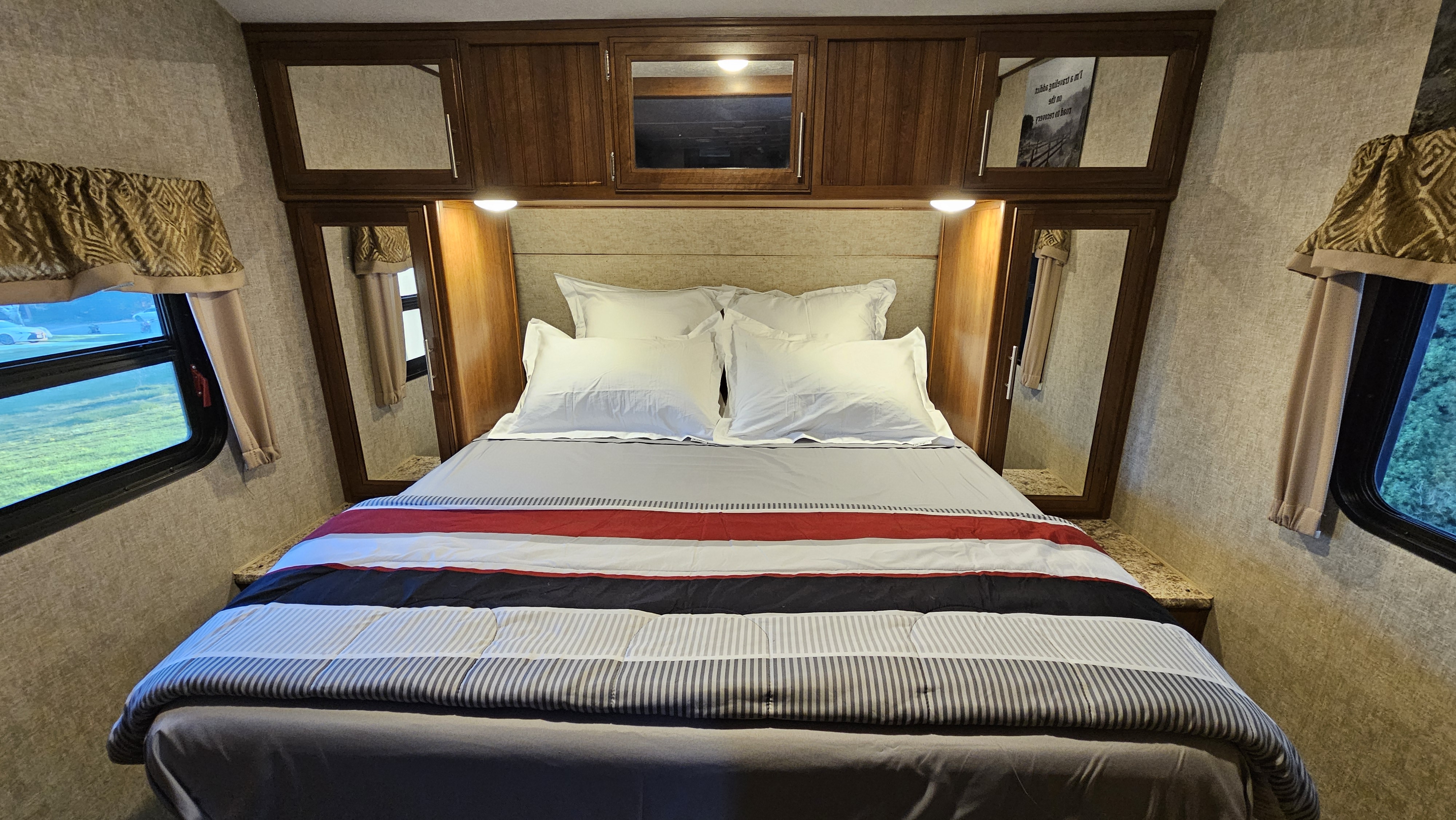 This inviting RV rental bedroom showcases a comfortable bed with striped comforter, white pillows, built-in cabinets, and side windows.. Forest River Tracer Air 2017