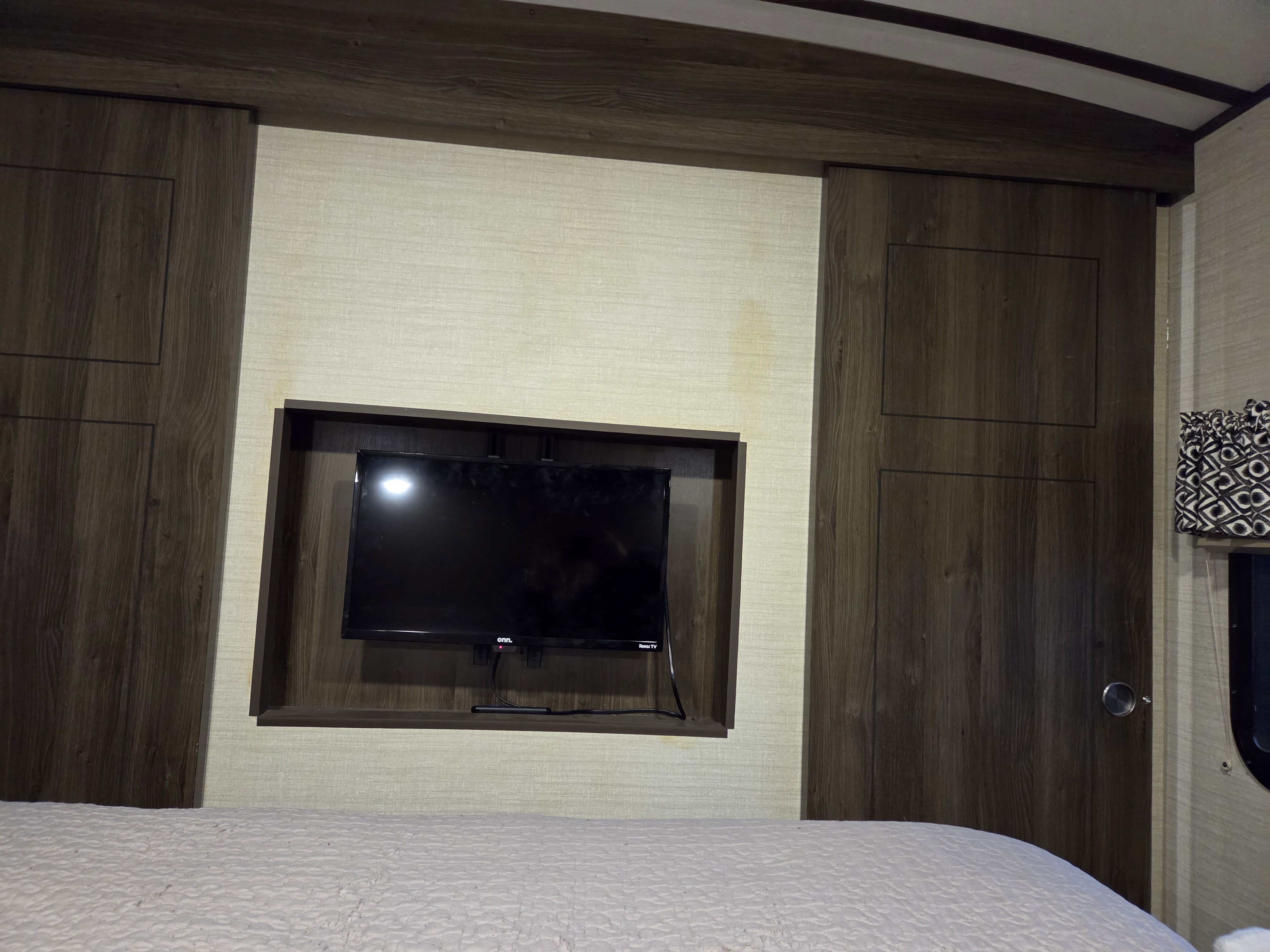 RV rental bedroom with mounted TV, sliding wardrobe doors, and bed. Wall stains are visible above the television.. Keystone RV Bullet Premier Ultra 2018