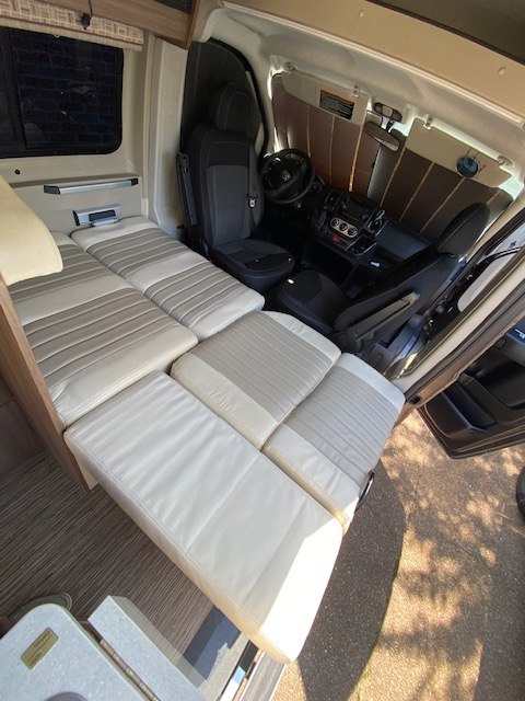 Spacious RV rental interior with versatile seating that converts into a comfortable bed, extending into the front cab area.. Winnebago Travato 2017