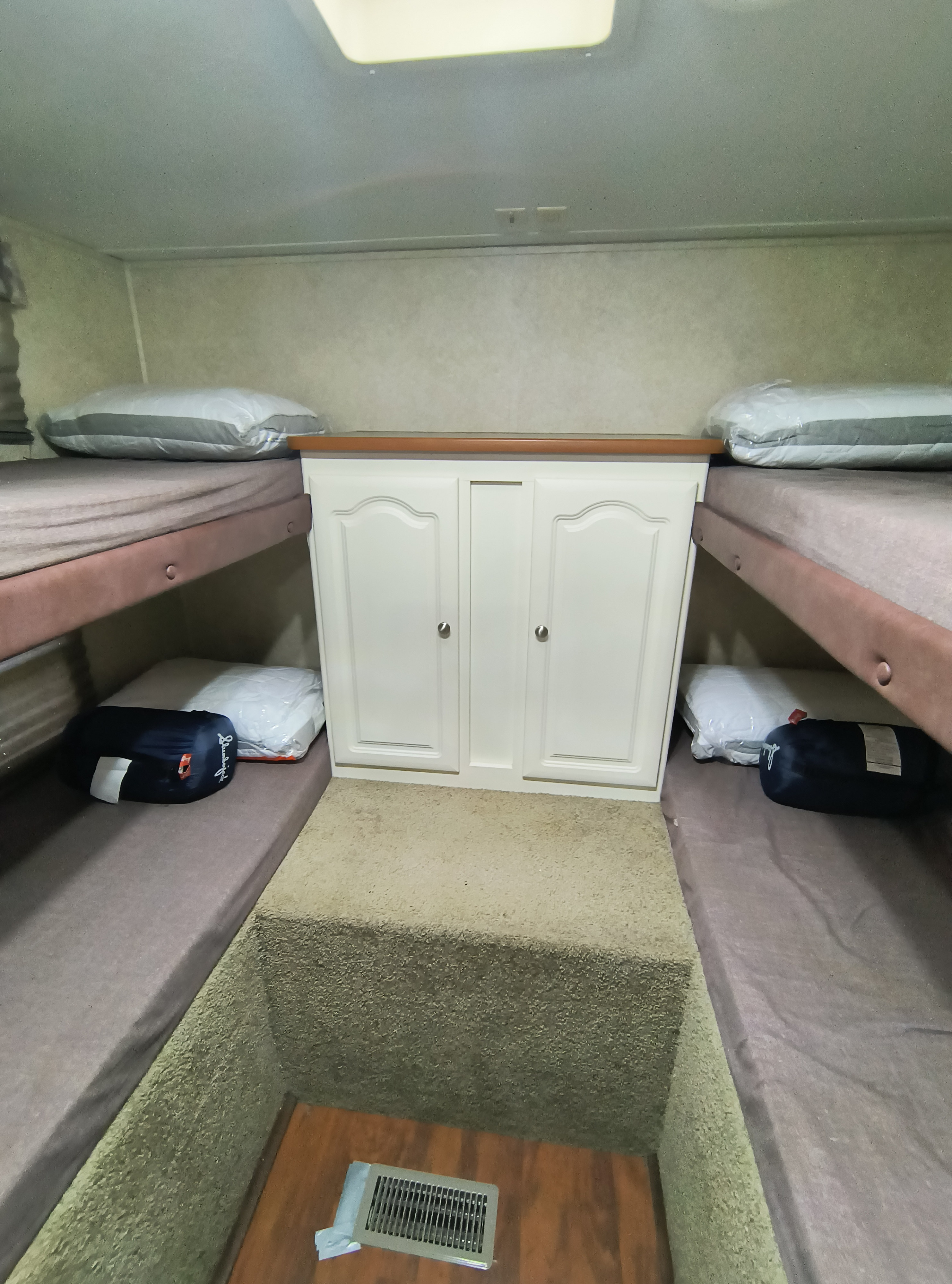 RV rental bunk beds: two sets of unmade beds flank a central storage cabinet, creating a compact sleeping area for travel.. Keystone RV Outback Sydney 2005
