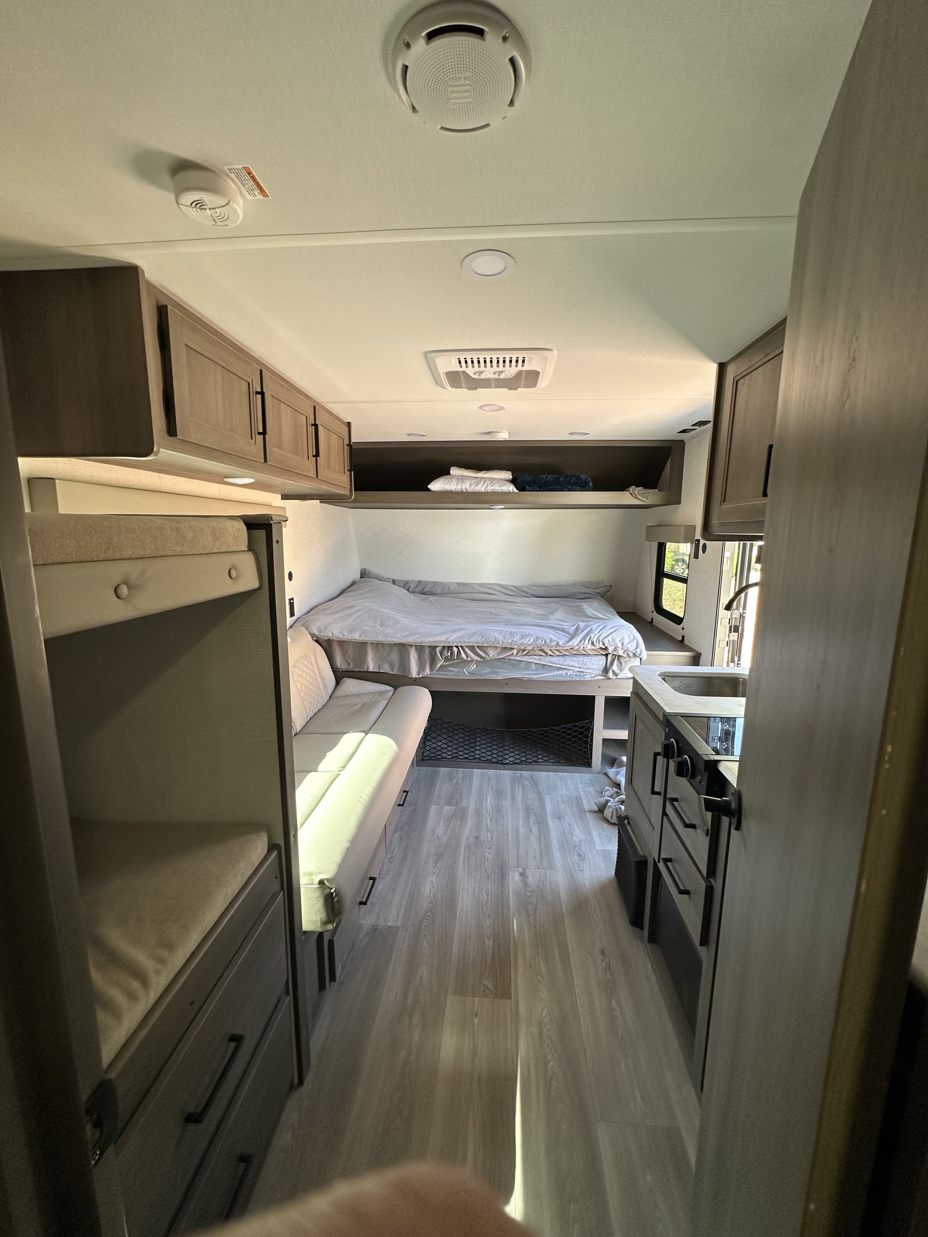 Bright RV rental interior showcasing bunk beds on the left, a main bed, and a compact kitchen counter on the right.. Transcend One 2025 2025