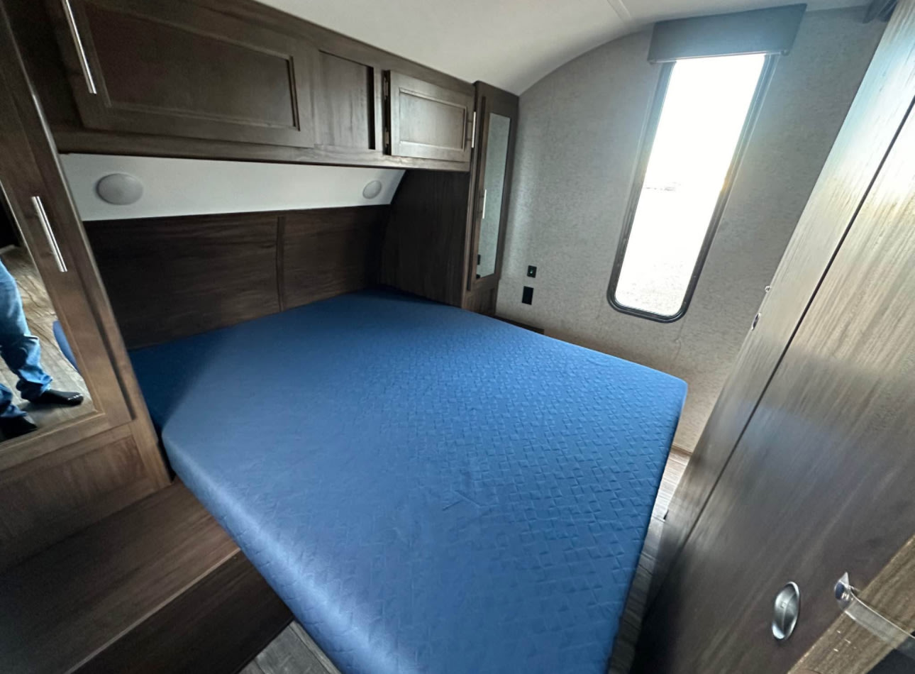Experience comfort in this RV rental bedroom. Features a blue bed, dark wood overhead cabinets, window & storage.. Forest River Cherokee Grey Wolf 2018