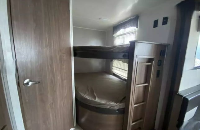 RV rental interior: cozy bunk beds with mattresses, a window, and a door for comfortable sleeping space.. Heartland RVs Trail Runner SLE 2018