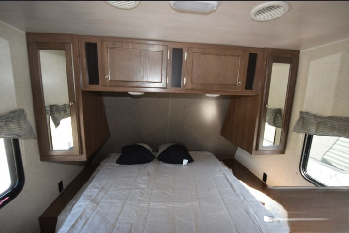 Spacious RV rental bedroom featuring a bed, overhead wooden cabinets with mirrors, and side windows with blinds.. Heartland RVs Trail Runner SLE 2018