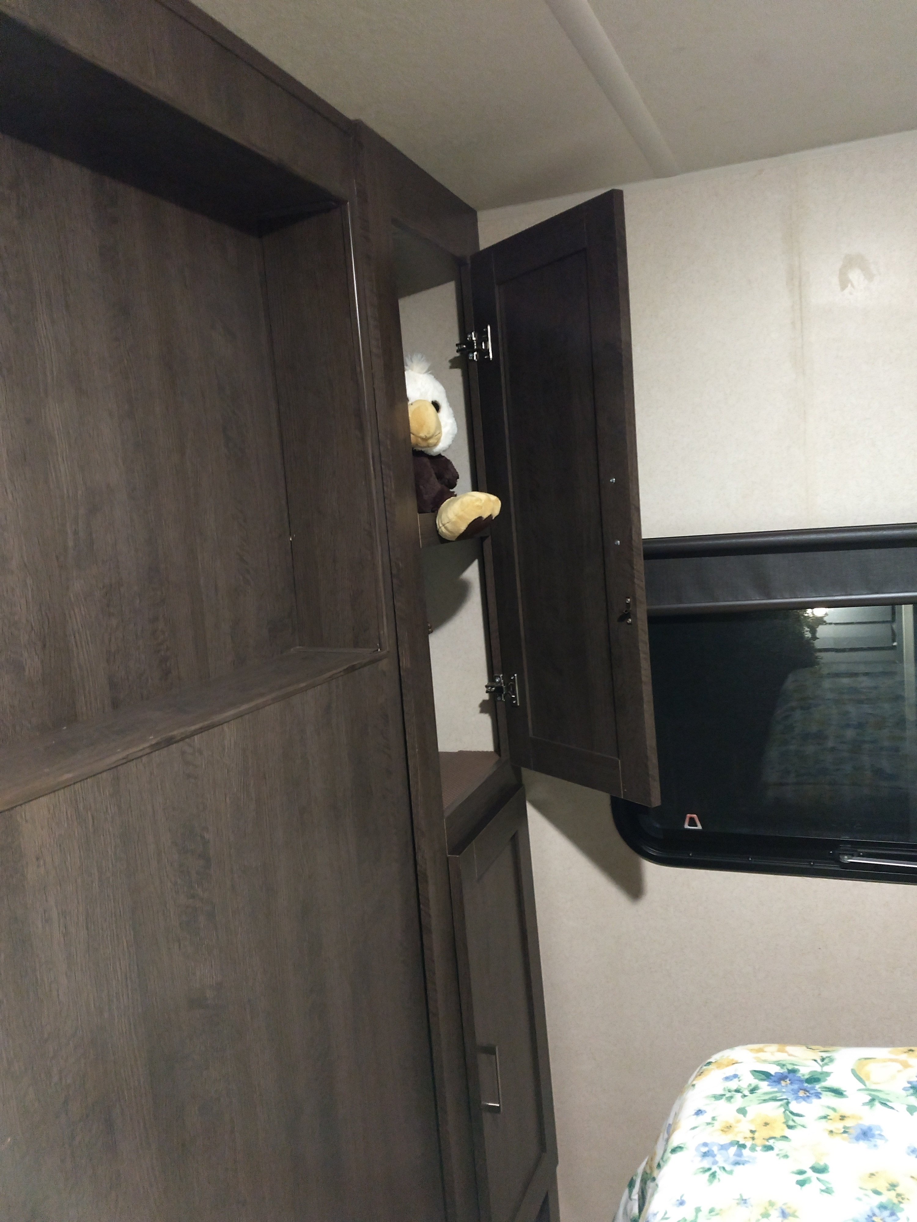 Modern RV rental interior with dark wood cabinets, an open one revealing a plush eagle, and a window with a bed.. Forest River Salem 2018