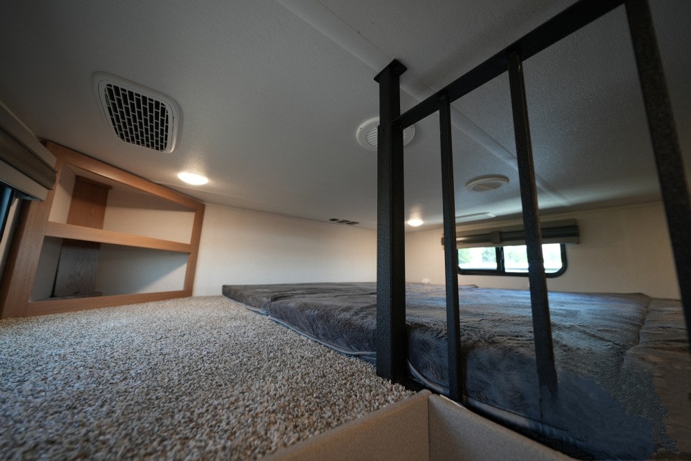 RV rental bunk loft: carpeted floor, plush mattress, safety railing, built-in shelves, and windows.. Prime Time Sanibel 2023