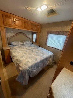 Cozy RV rental bedroom with a queen bed, overhead storage, and a window with blinds, ideal for comfortable travel.. Dutchmen Dutchmen Motorhome 2007