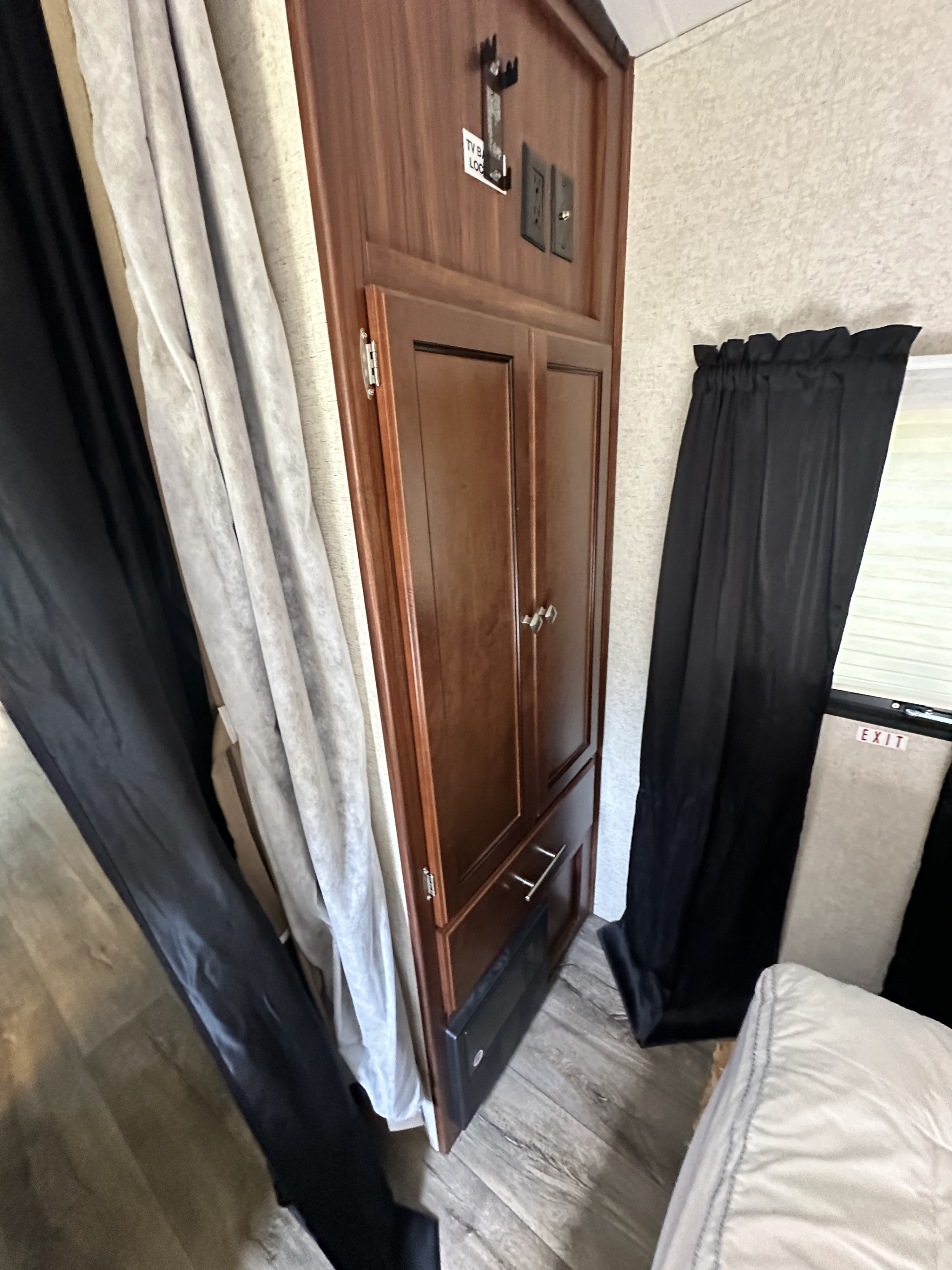 RV rental interior: wood cabinet with TV mount, outlets, and electric fireplace. Black & light curtains, EXIT window, wood floor.. Heartland RVs Mallard 2017