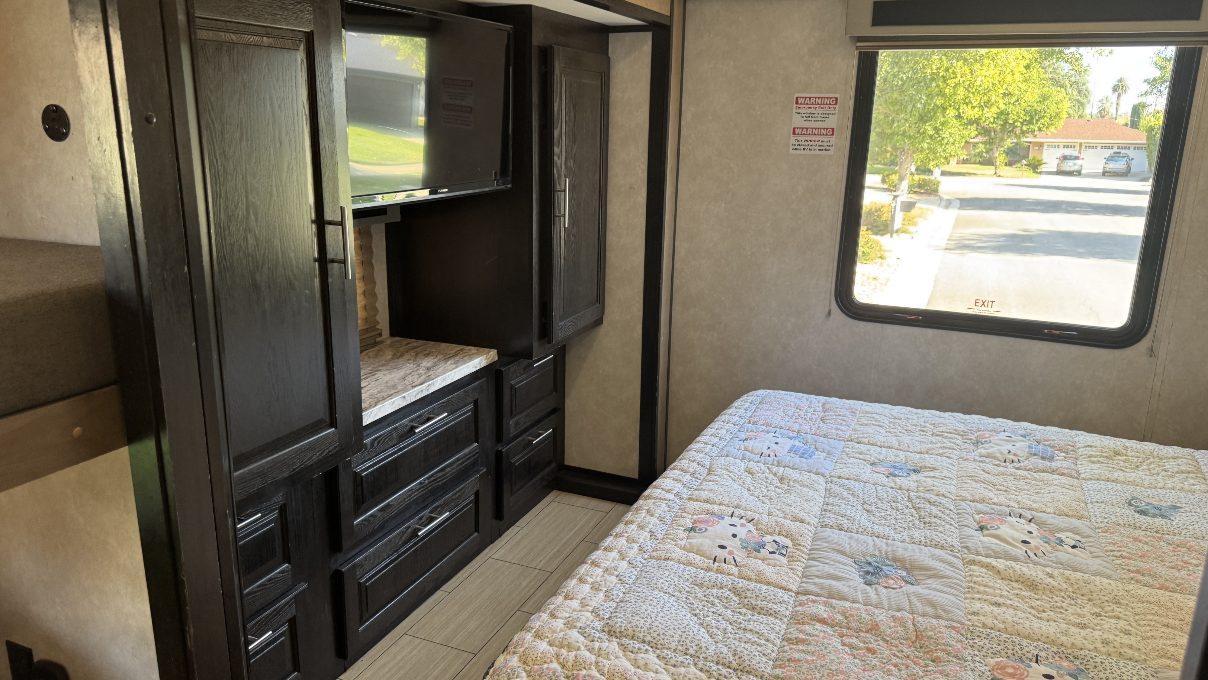 Inside an RV rental: a bedroom featuring dark wood cabinets with a TV, a bed with a patterned quilt, and an emergency exit window.. Forest River FR3 2020