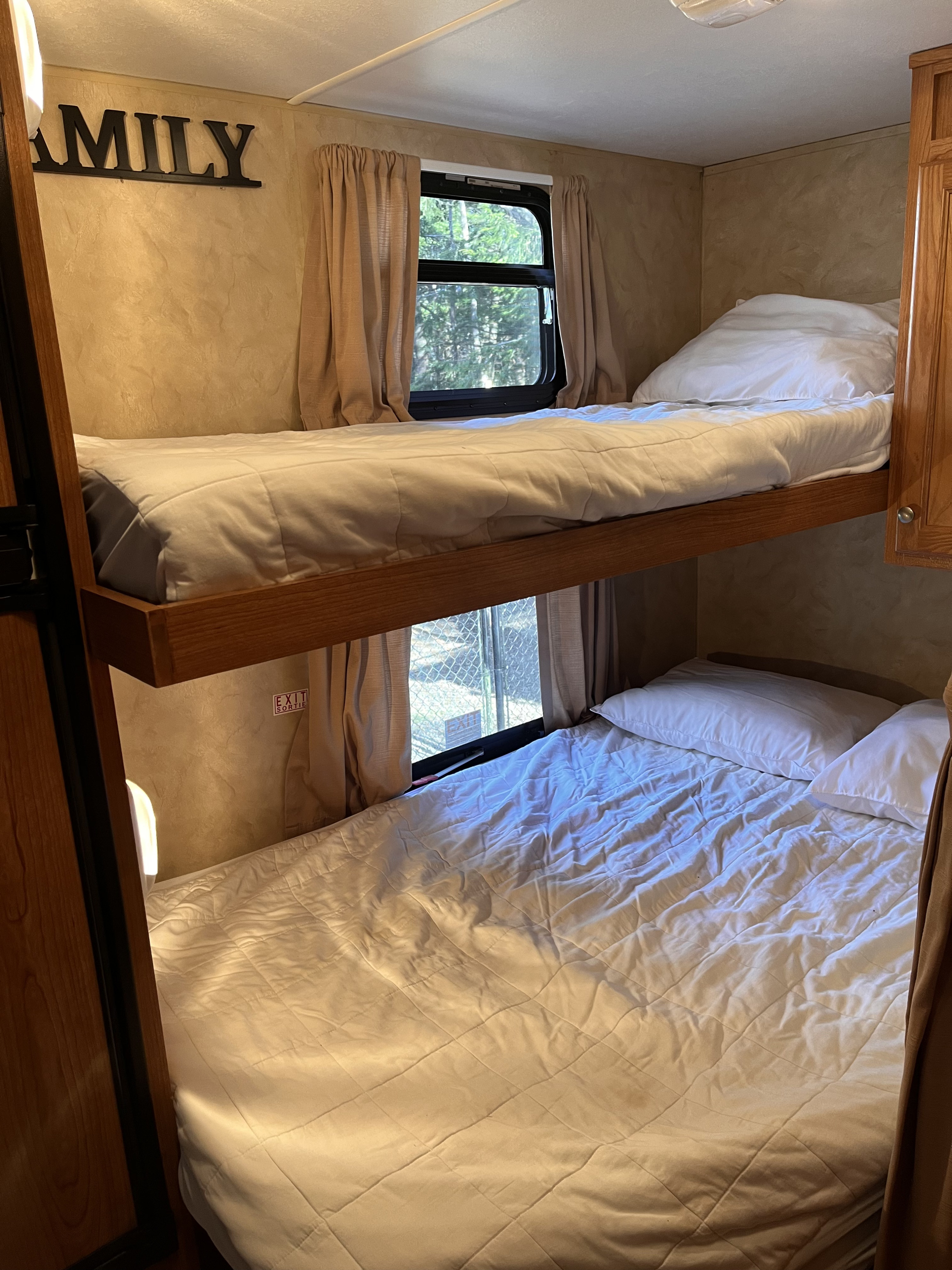 RV rental bunkroom: Two neatly made bunk beds with white bedding, windows with curtains, and a "FAMILY" wall sign.. R-Vision Trail Sport 2014