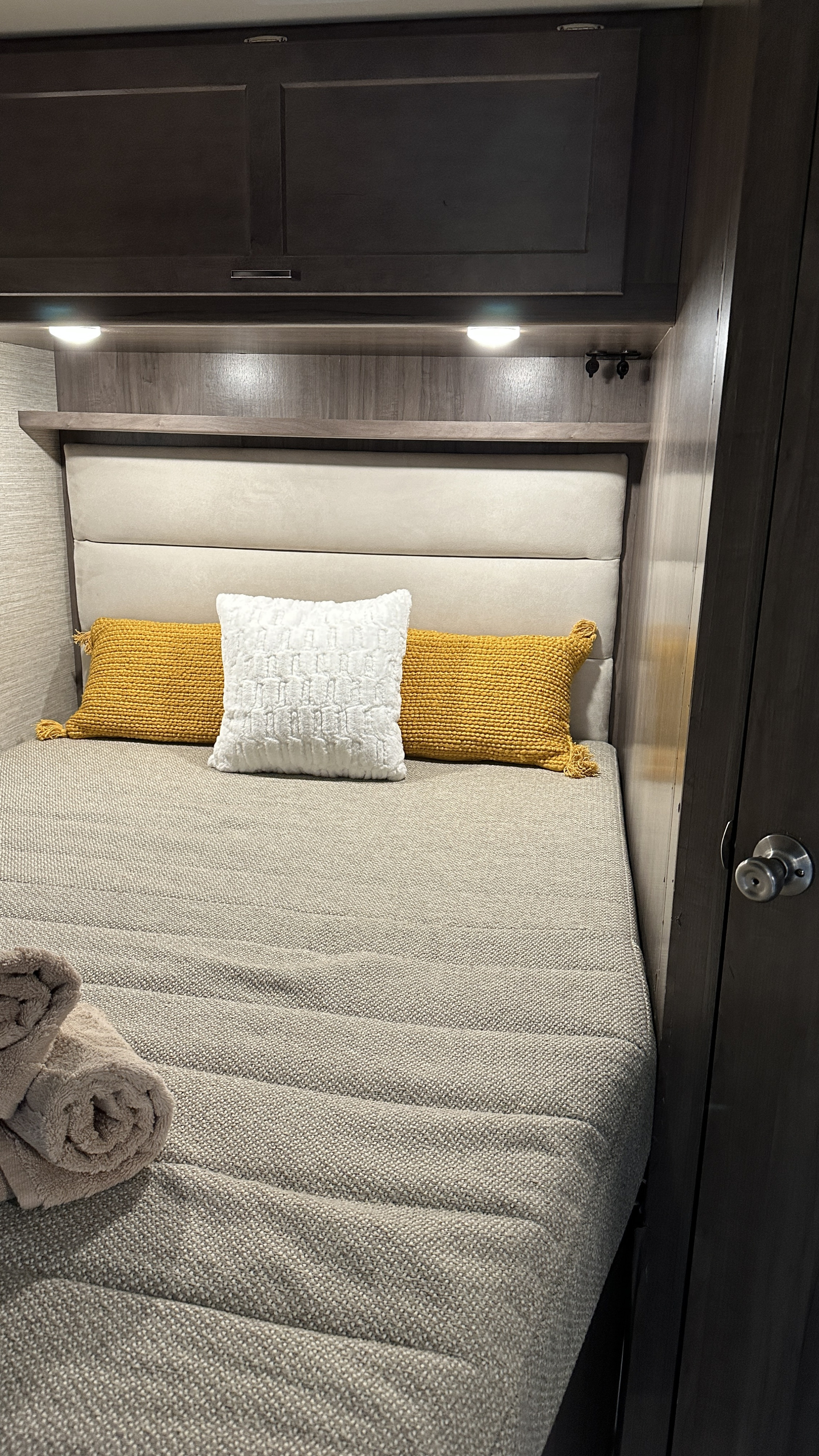An inviting RV rental bedroom with a gray textured bedspread, decorative pillows, and convenient overhead storage.. Winnebago Minnie Winnie 2023