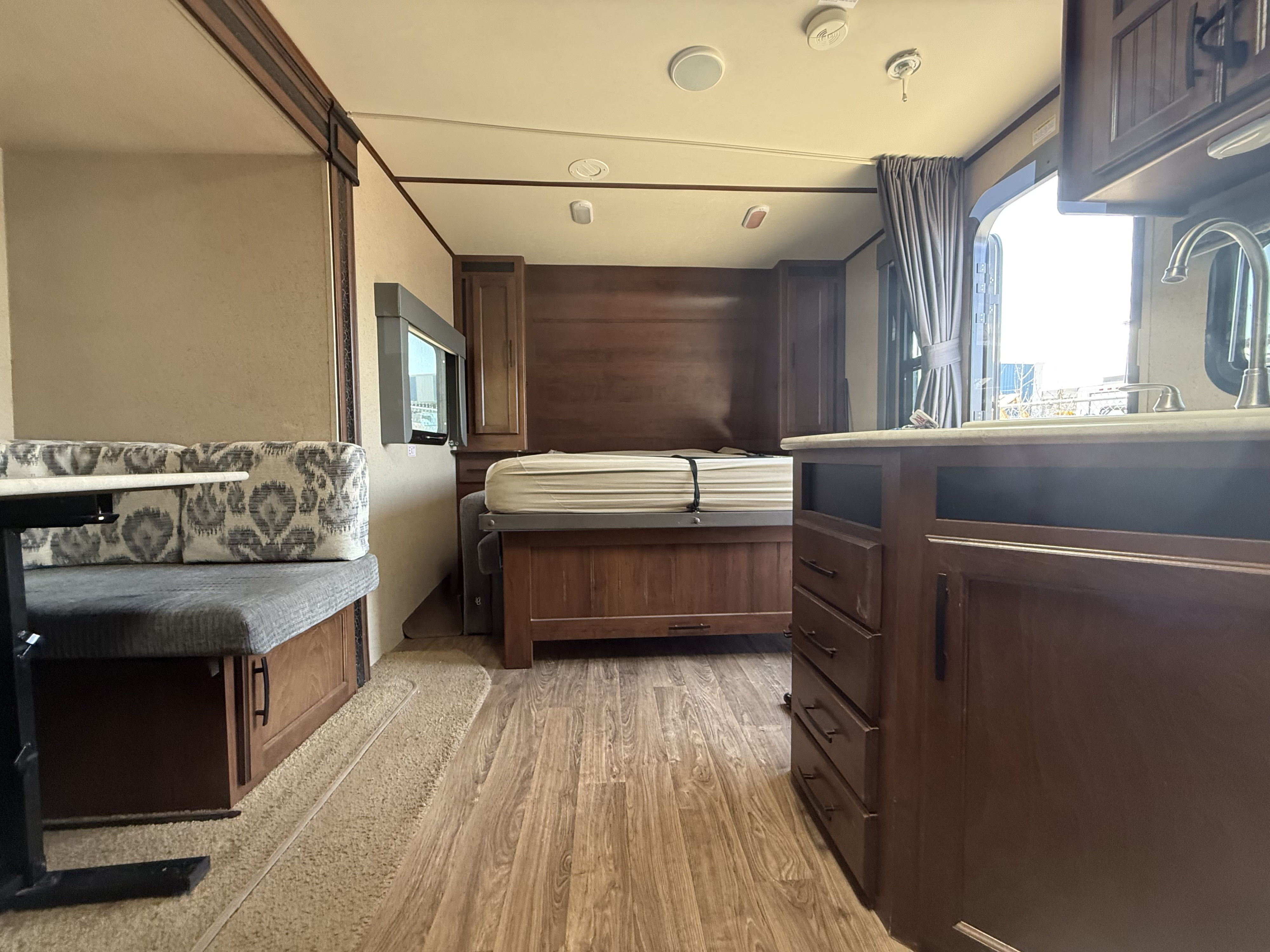 Inside this rv rental: dinette on left, bed ahead, and kitchen on right. Wood tones and light walls create a warm, functional space.. Jayco White Hawk Ultra Lite 2015