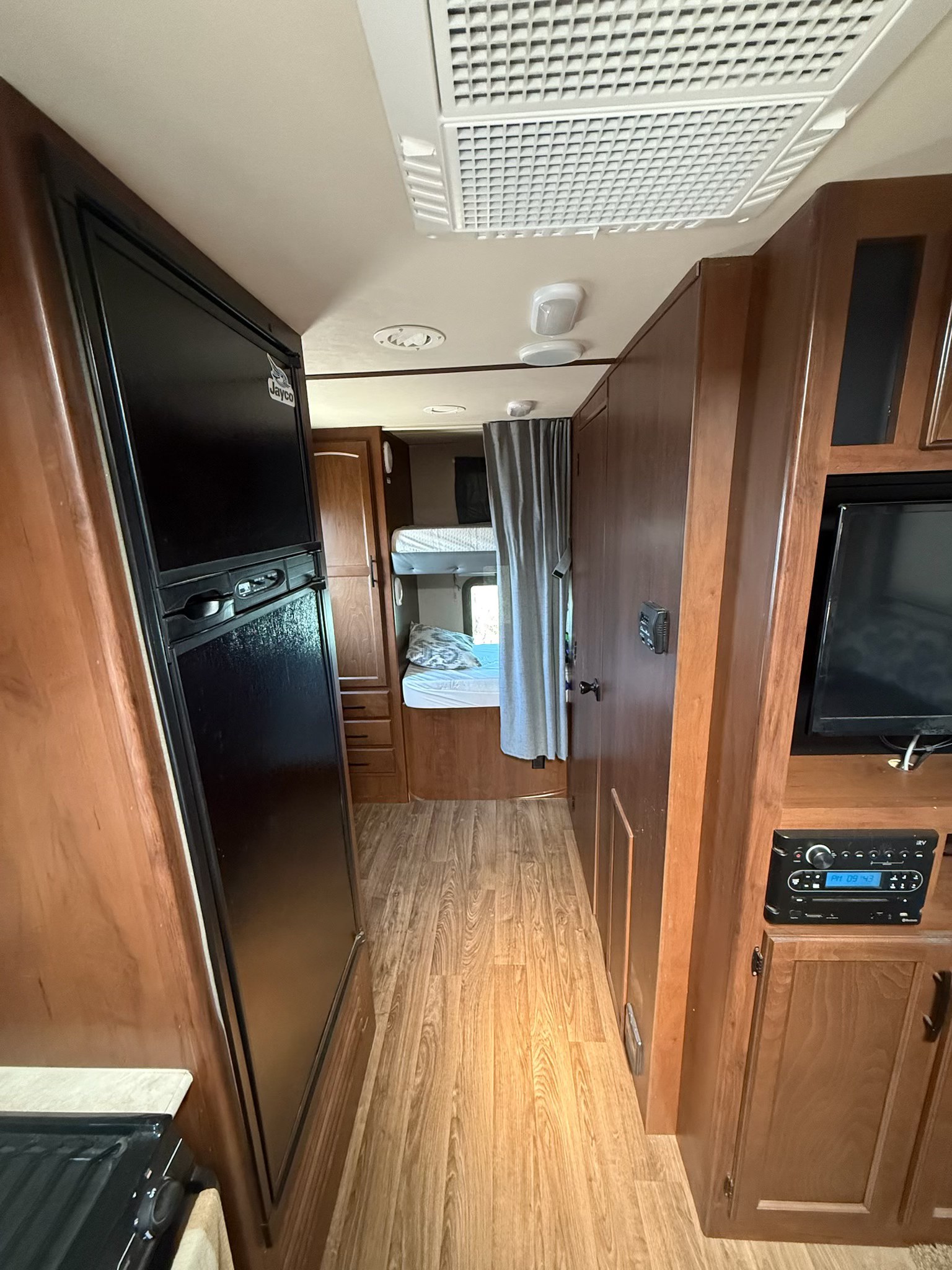 Inside an RV rental: Compact living area with a fridge, entertainment center, and bunk beds visible down the aisle. Great for family trips.. Jayco White Hawk Ultra Lite 2015