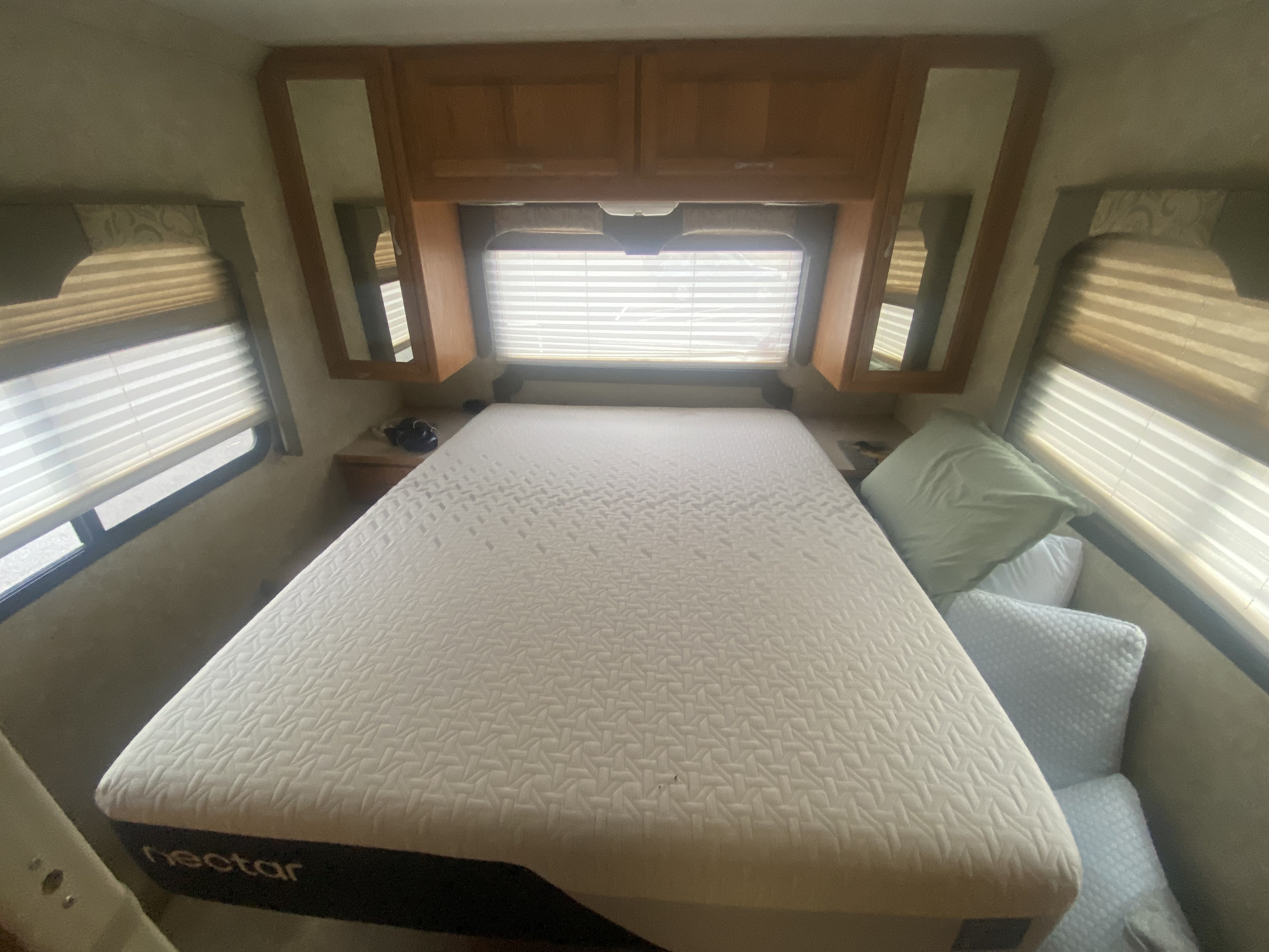 Inside an RV rental, a comfy bedroom with a large Nectar mattress, window blinds, and wood cabinets.. Four Winds Hurricane 2004