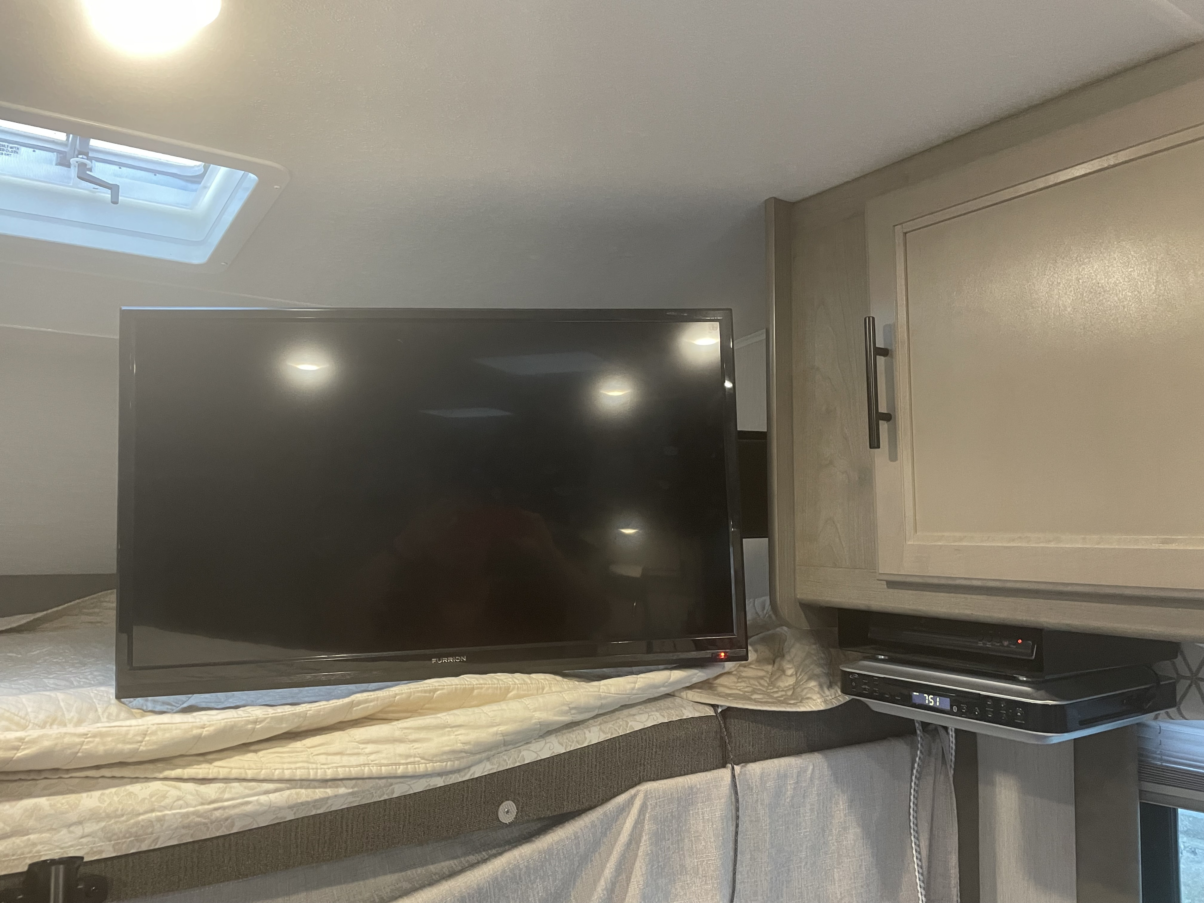 RV rental interior: A Furrion TV on the bed, with a mounted entertainment system unit and overhead cabinet.. Coachmen Freelander 26DS 2020